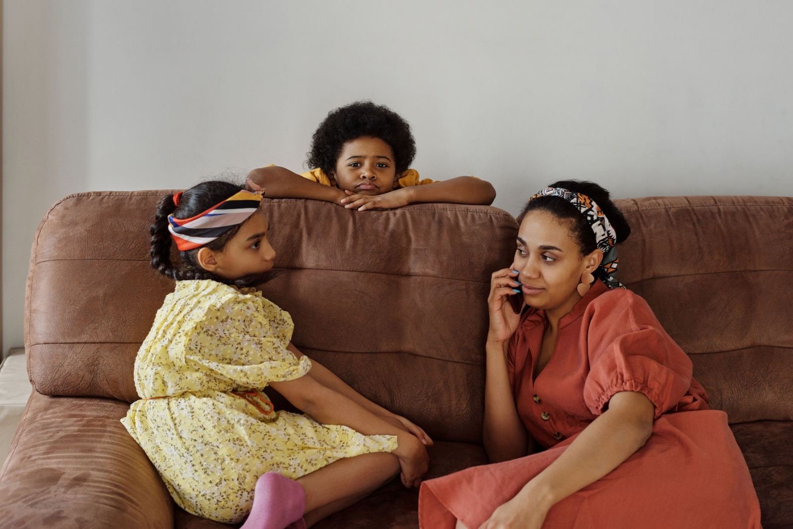 A woman on a phone call sits on a sofa with two children