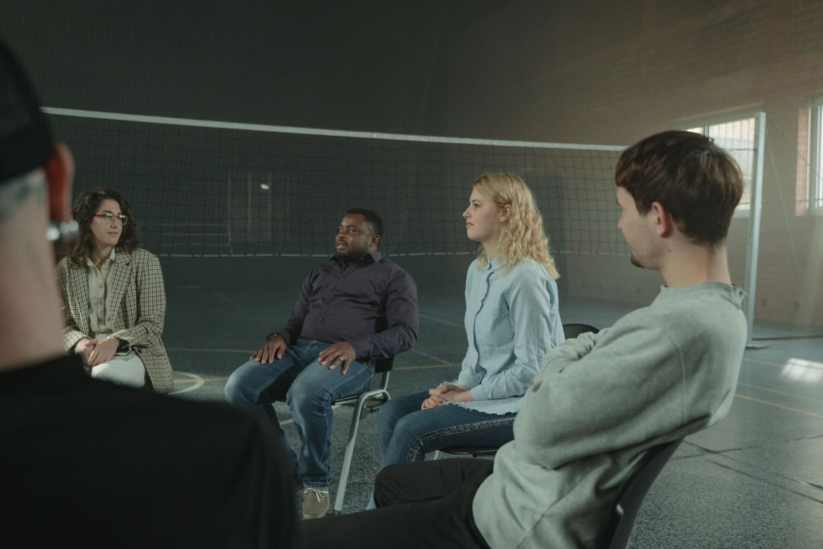 Four adults sit in a circle of chairs having a group conversation in a large room