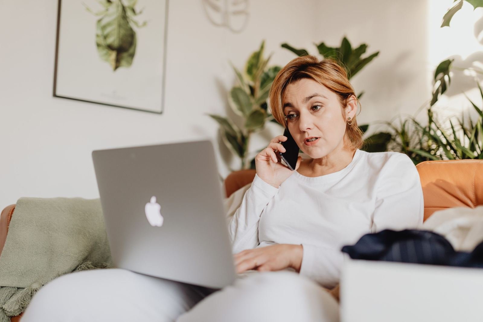 A woman talks on a mobile phone while sitting on a sofa with a laptop