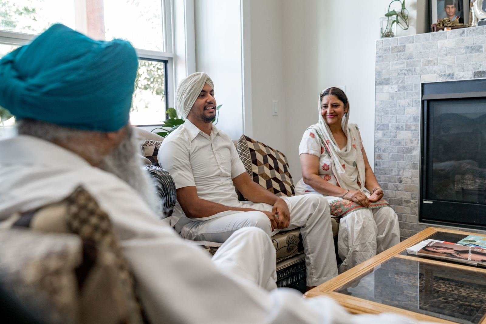Three people in traditional Indian attire sit and talk in a living room