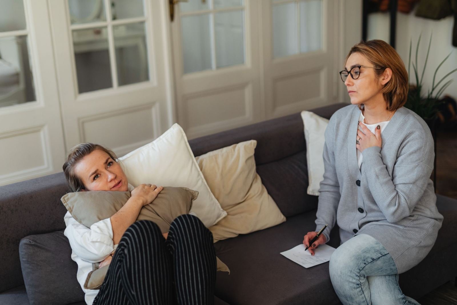 A woman lying on a sofa talks with a professional holding a pen and paper