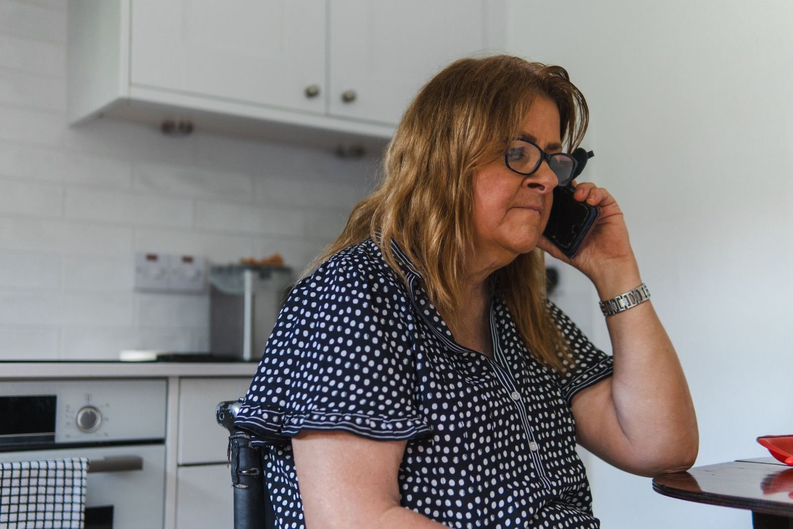 A woman with glasses talks on a mobile phone in a bright kitchen