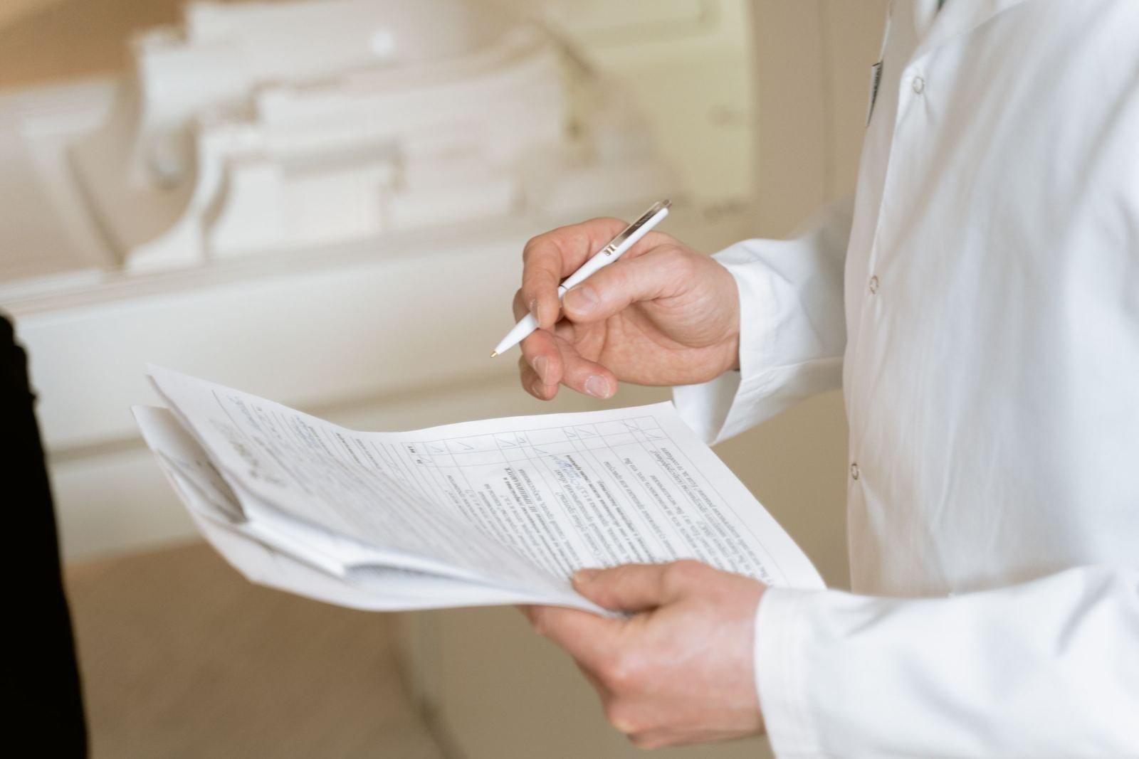 A person in a white lab coat holds a pen and reviews paperwork