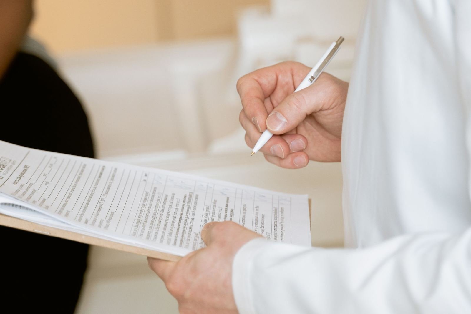 A healthcare provider in a white coat holds a clipboard and pen