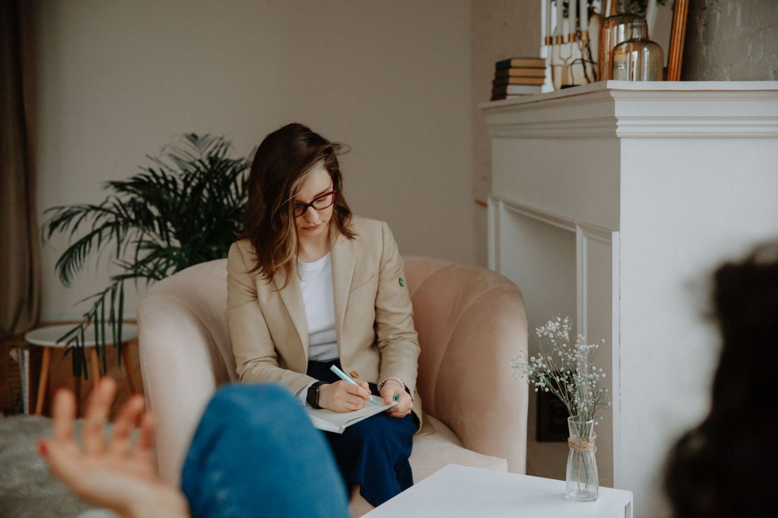 A counselor in a tan blazer takes notes while listening to a client