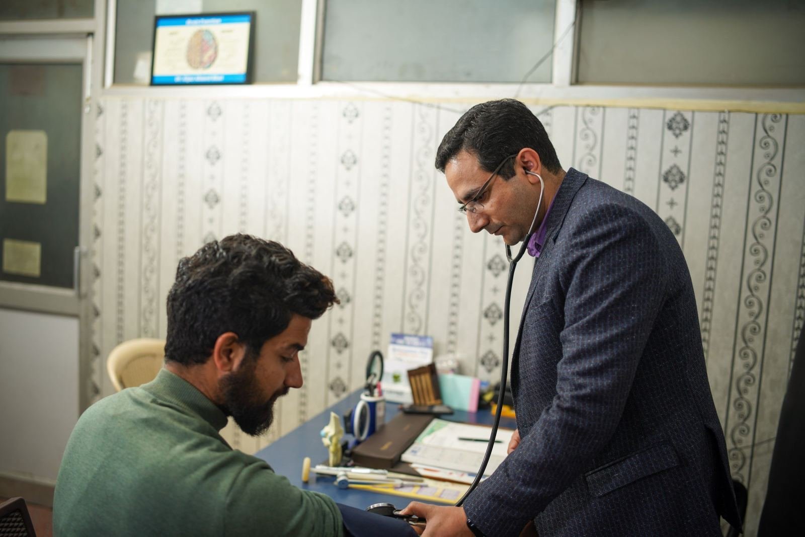 A doctor uses a stethoscope to examine a man's arm in a medical office