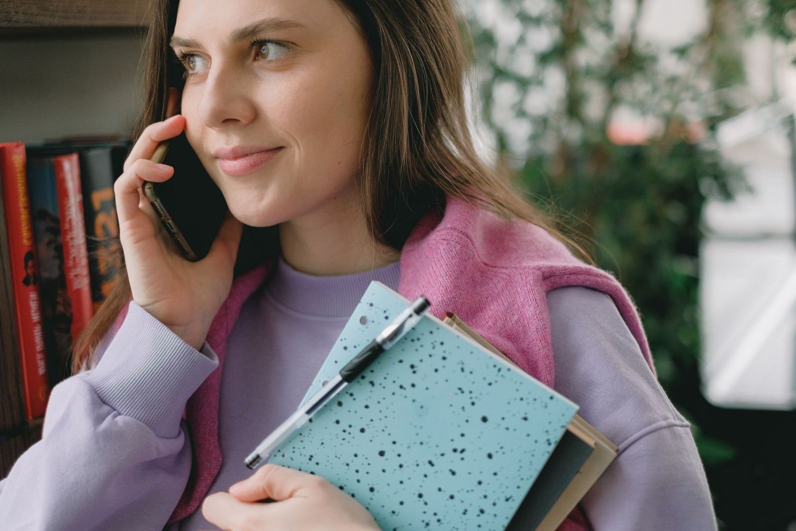 A woman on a phone call holding a blue speckled notebook and pen