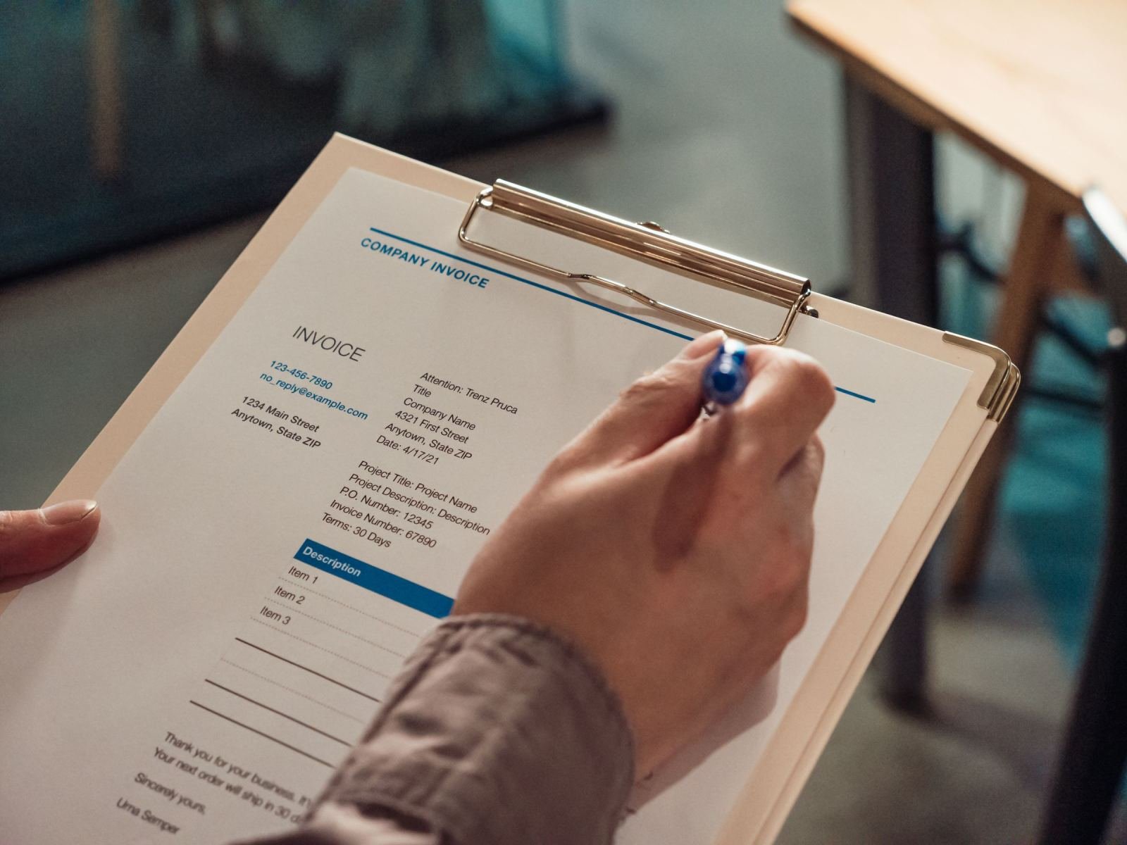 A person using a blue pen to write on an invoice on a clipboard