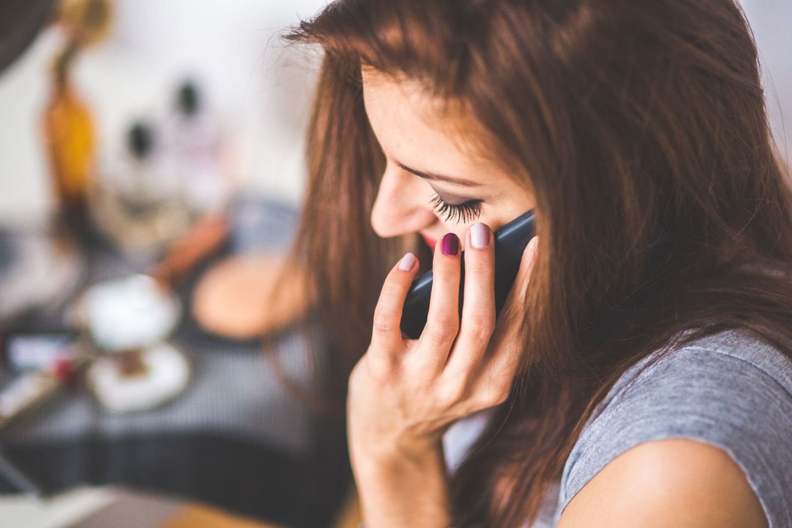 A woman with long brown hair is smiling as she talks on a phone.