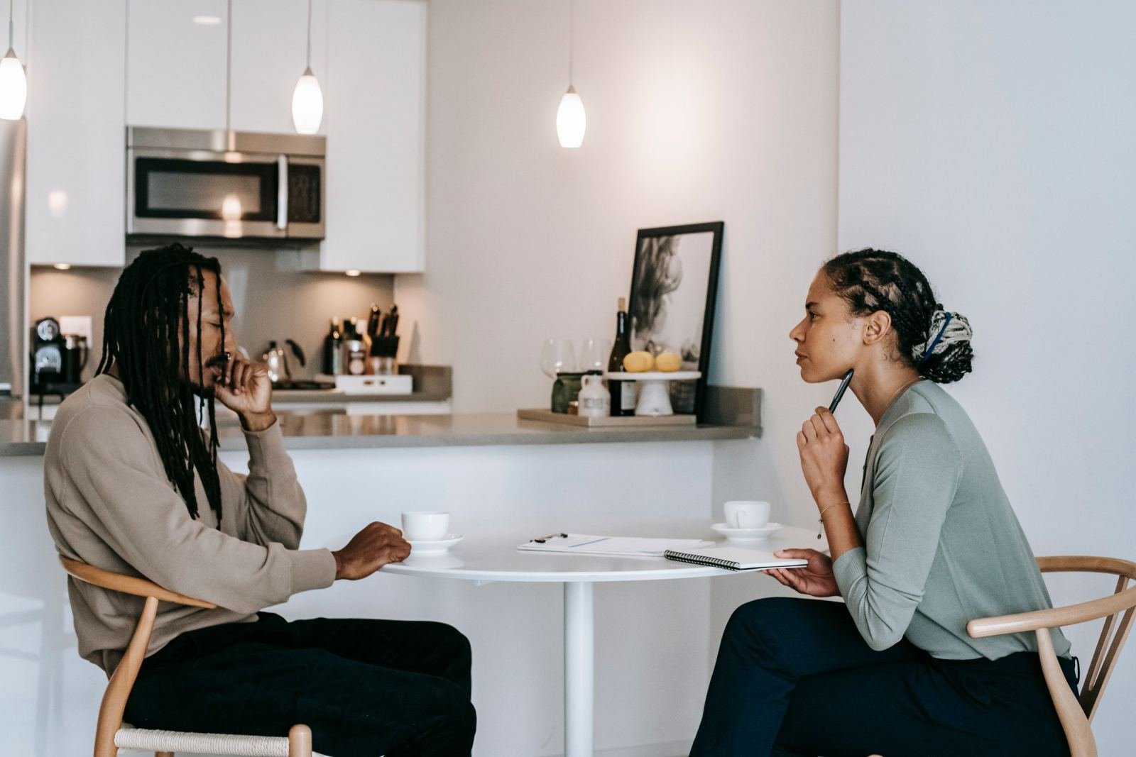 A man and woman sit at a white table talking in a bright room