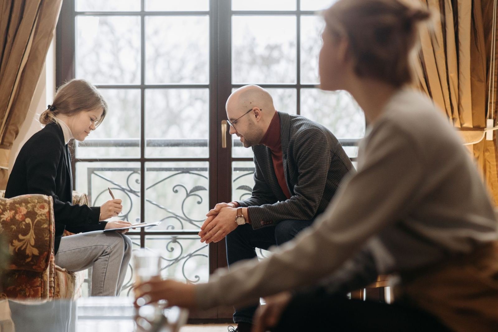 In a bright office, a clinician with a clipboard talks with two people.