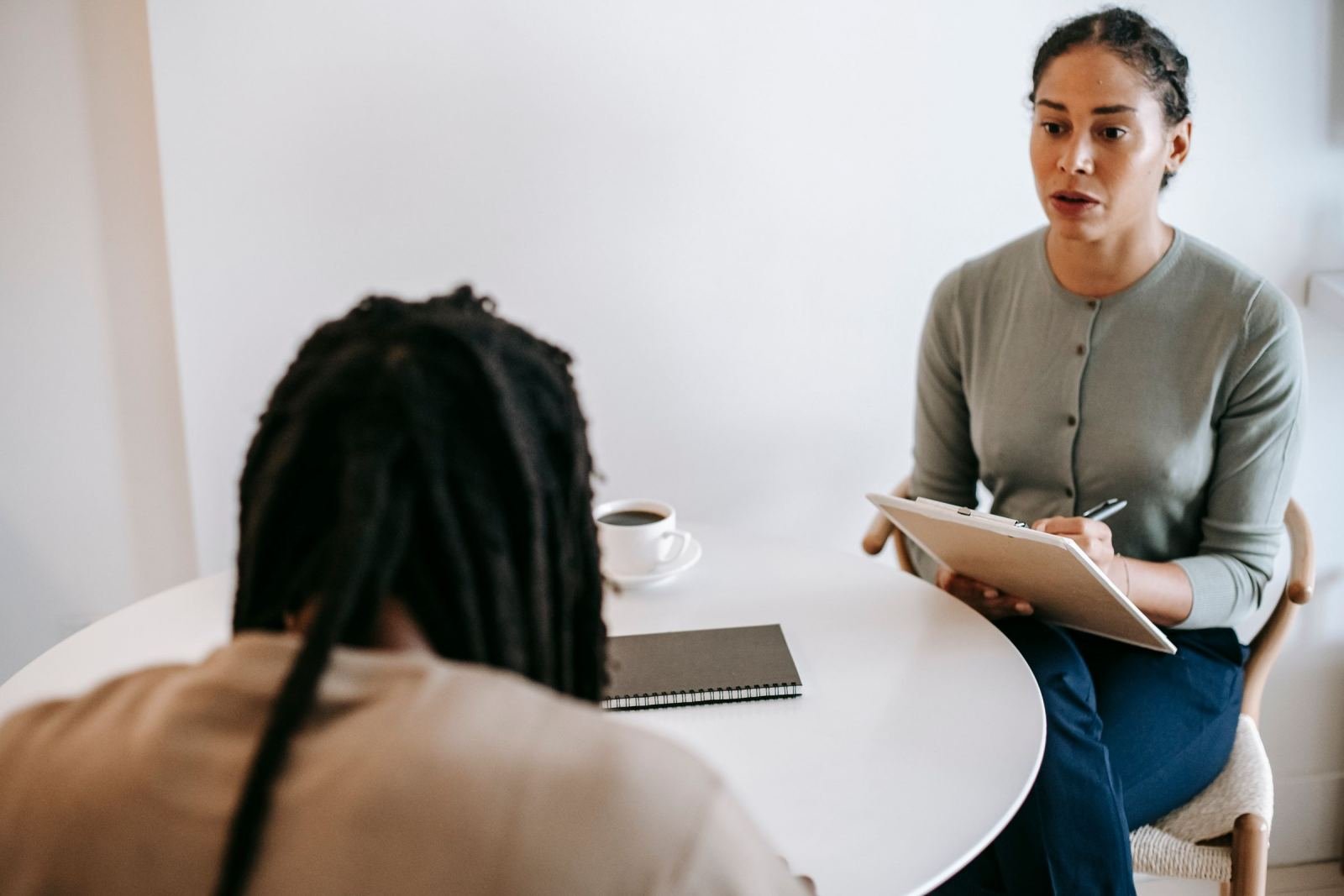 A clinician with a clipboard listens to a client at a white round table
