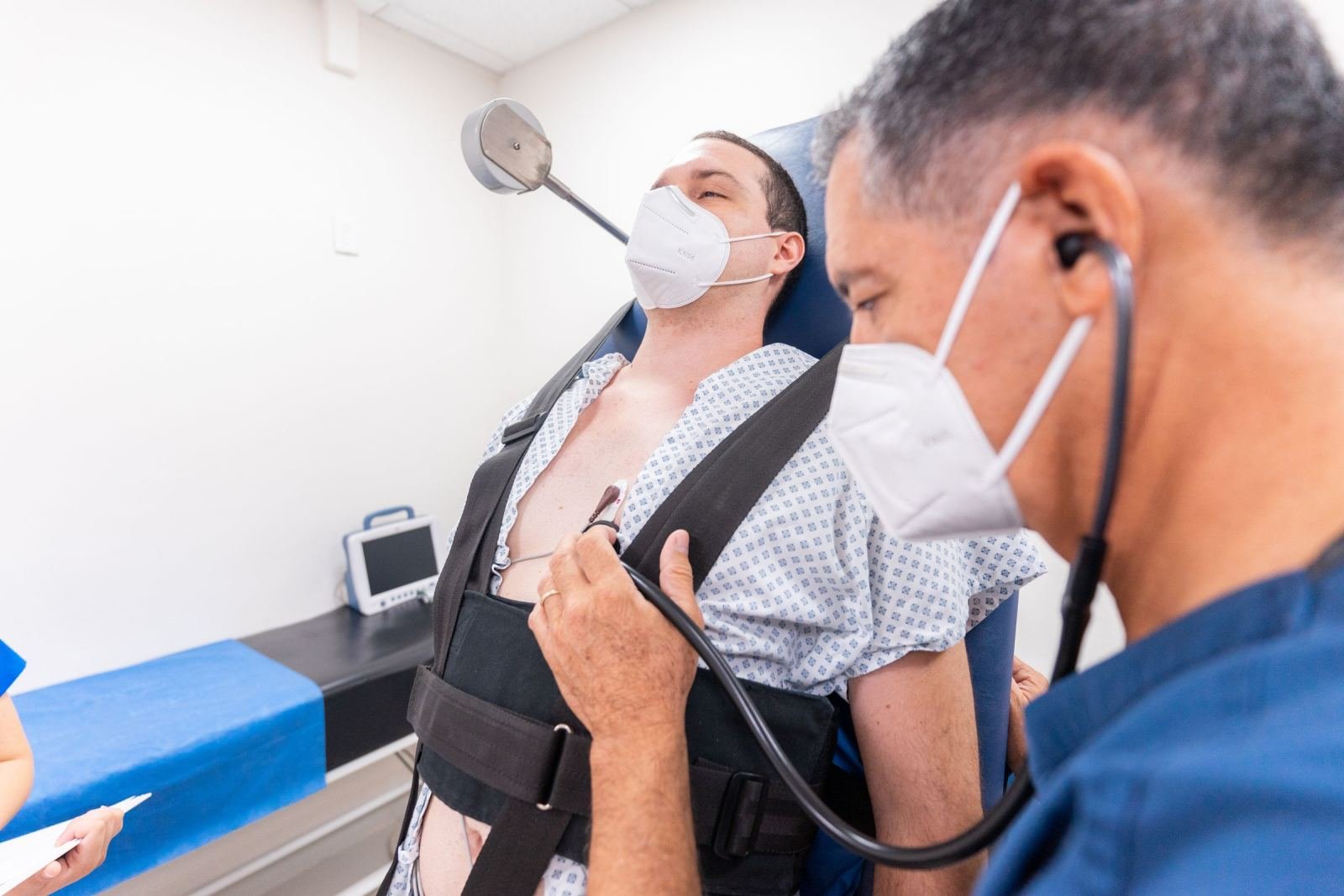 A clinician listens to a patient's chest with a stethoscope in a well-lit clinic.