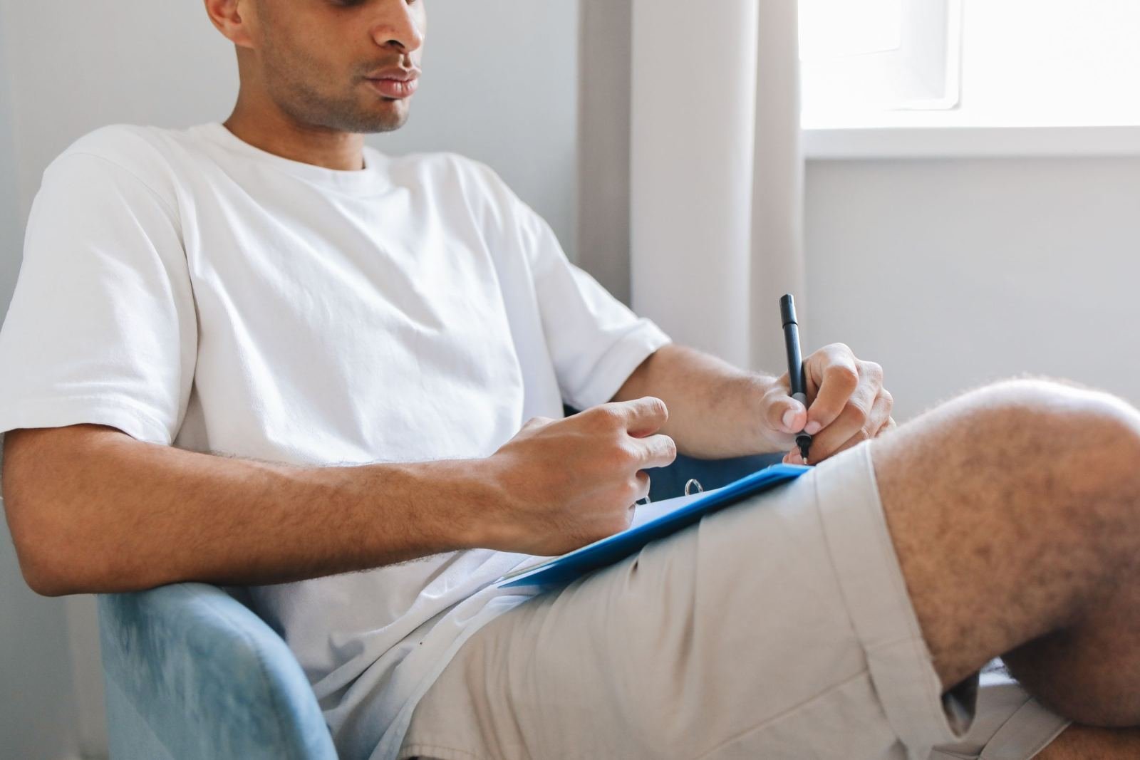 A man in a white t-shirt writes on a blue clipboard