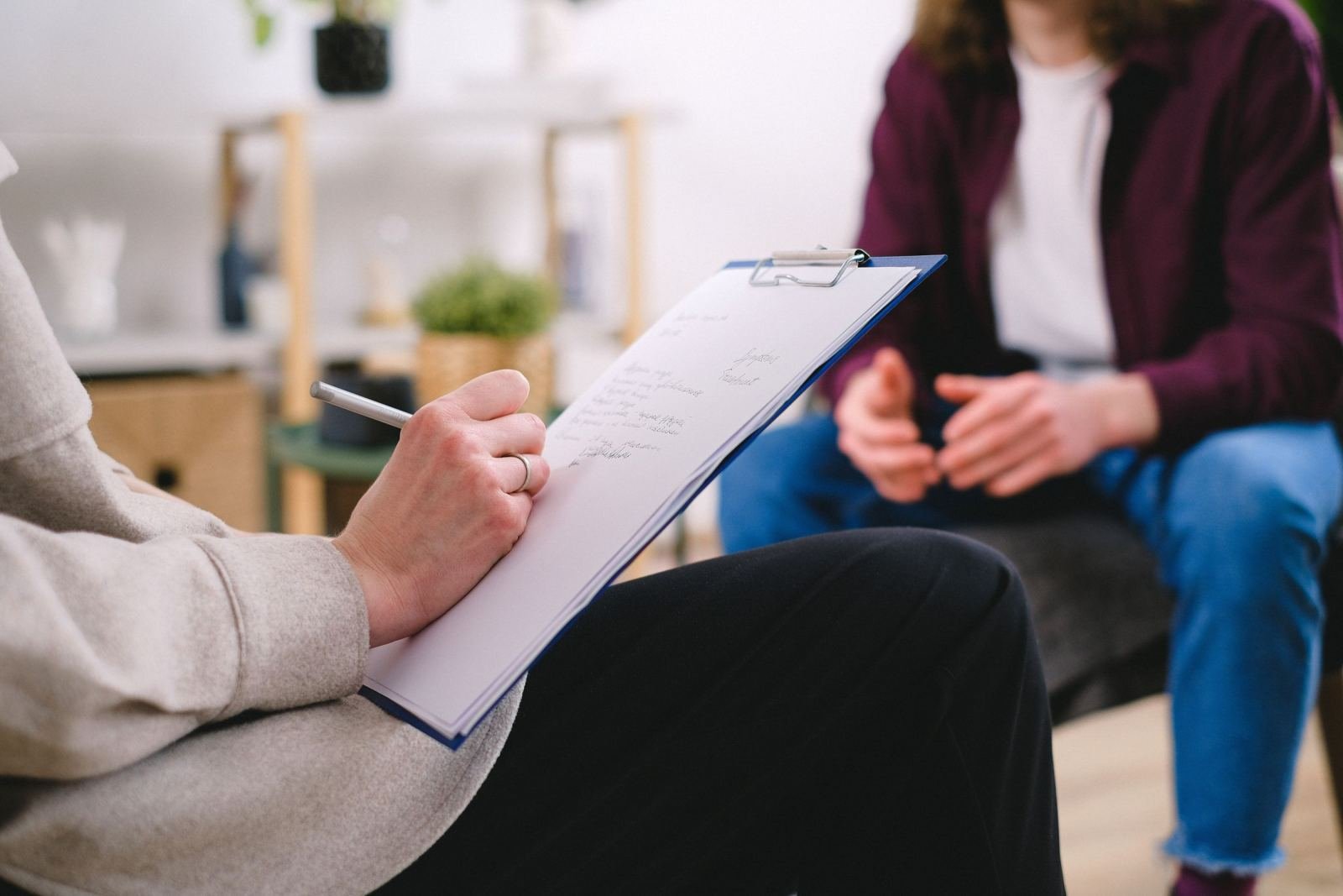 A clinician writes on a clipboard while talking with a client in a bright room
