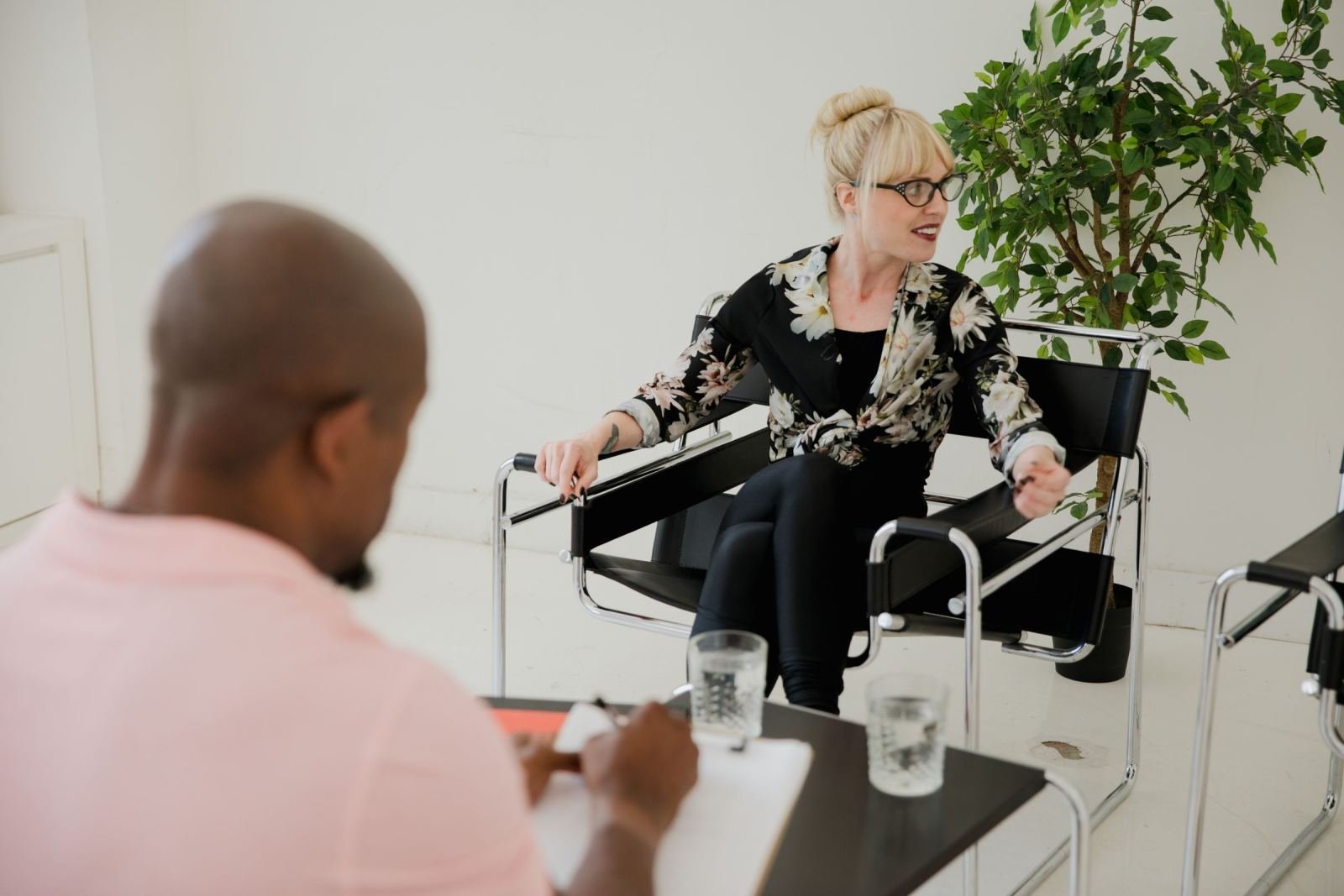 A woman in glasses speaks with a man who is taking notes on a clipboard
