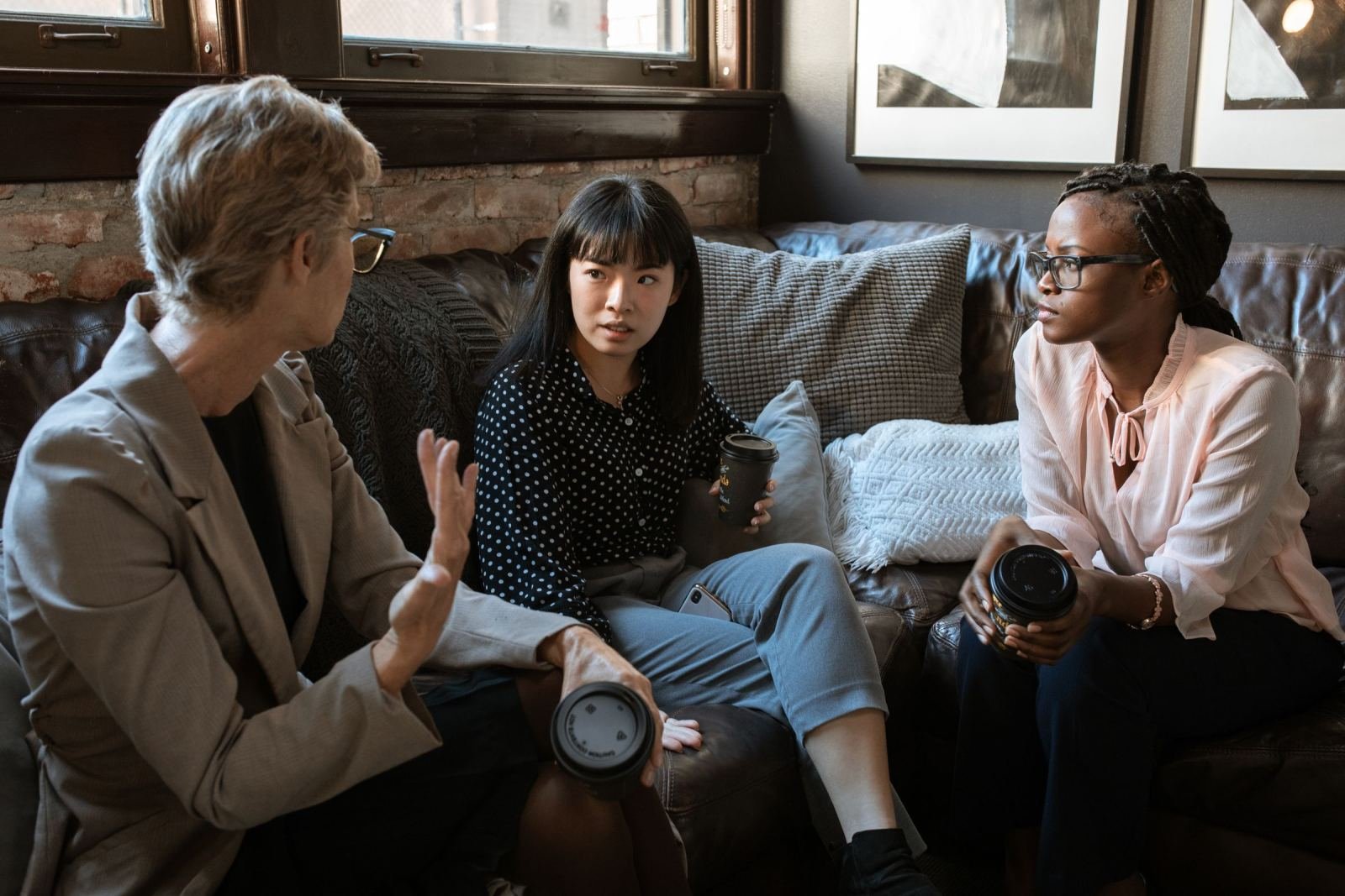 Three people talking and holding coffee cups while sitting on a leather sofa