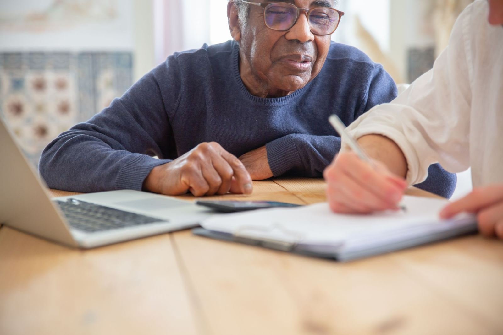 One man watches while someone else marks a clipboard on a wooden table.