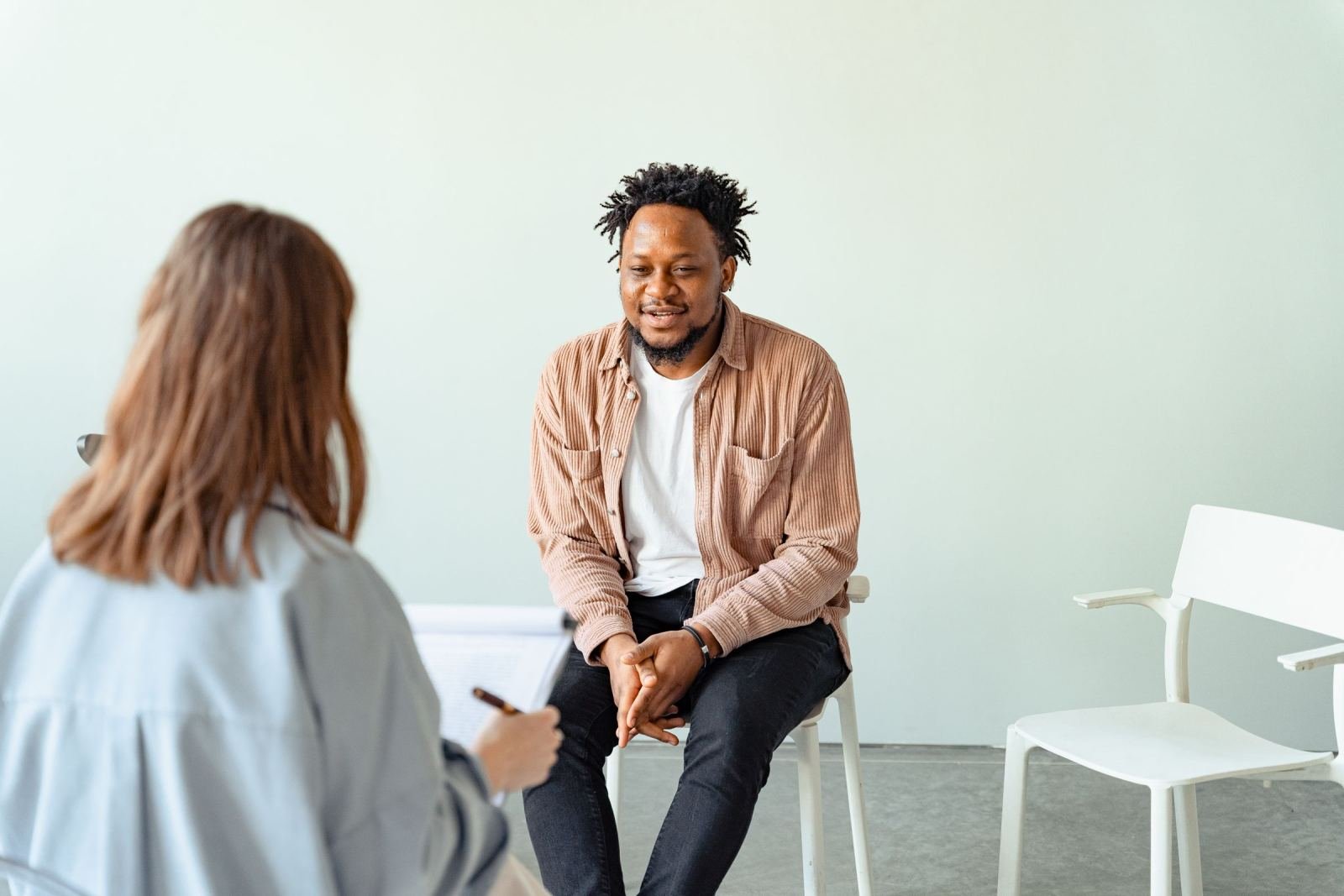 A man sits in a white chair talking to a provider with a clipboard