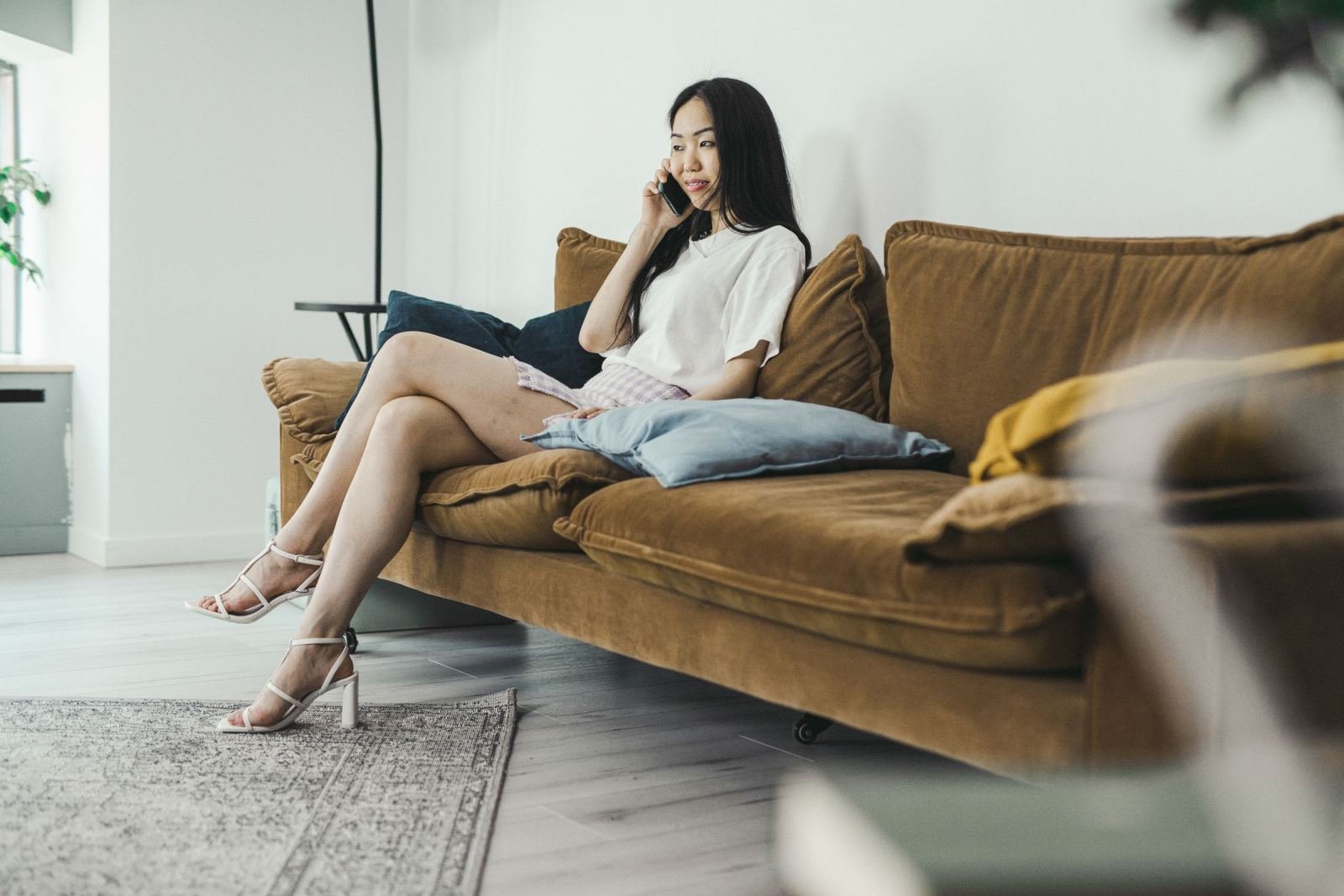 A woman talks on her phone while sitting on a brown couch