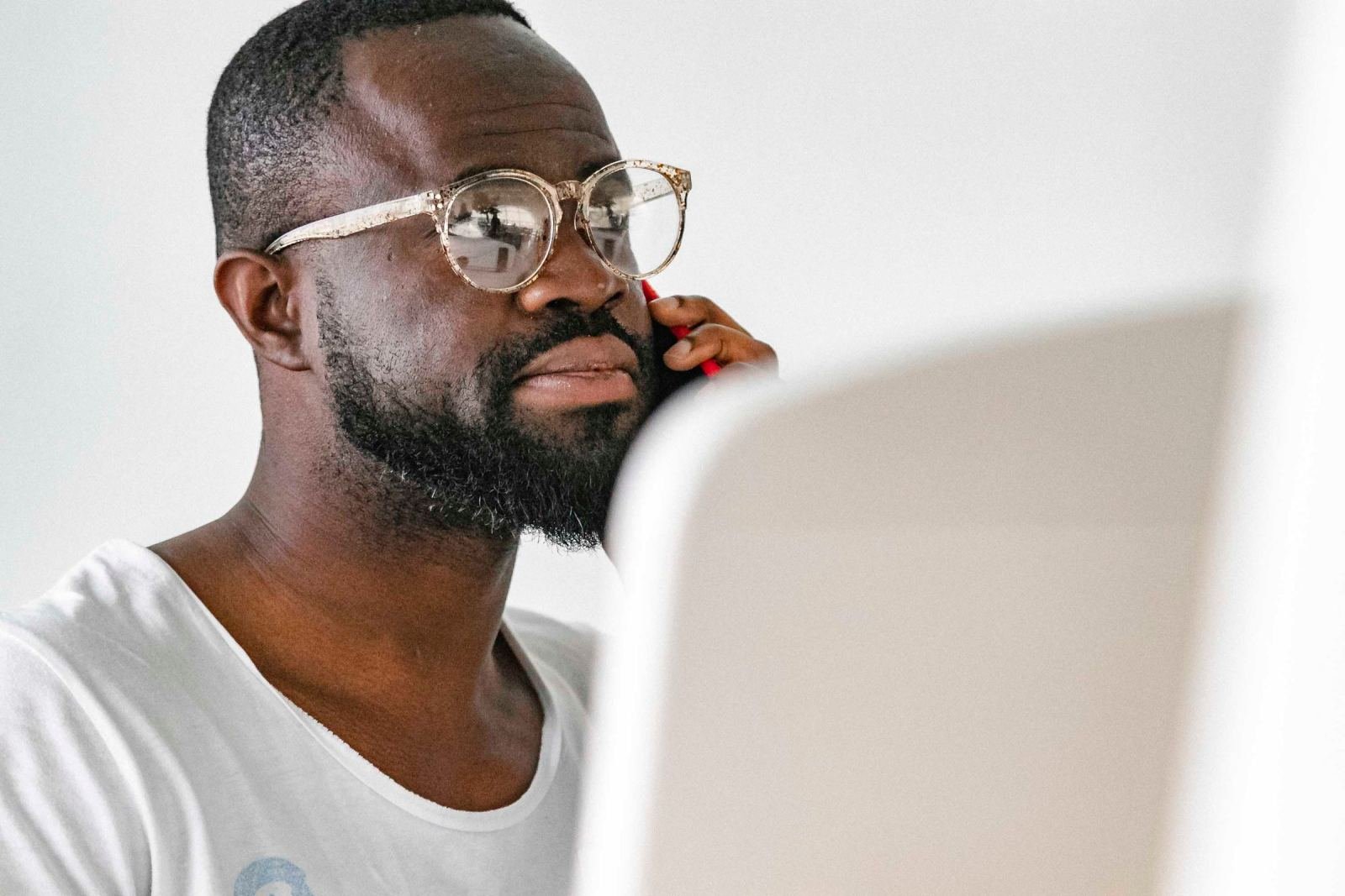 A man with glasses and a beard talks on a red phone