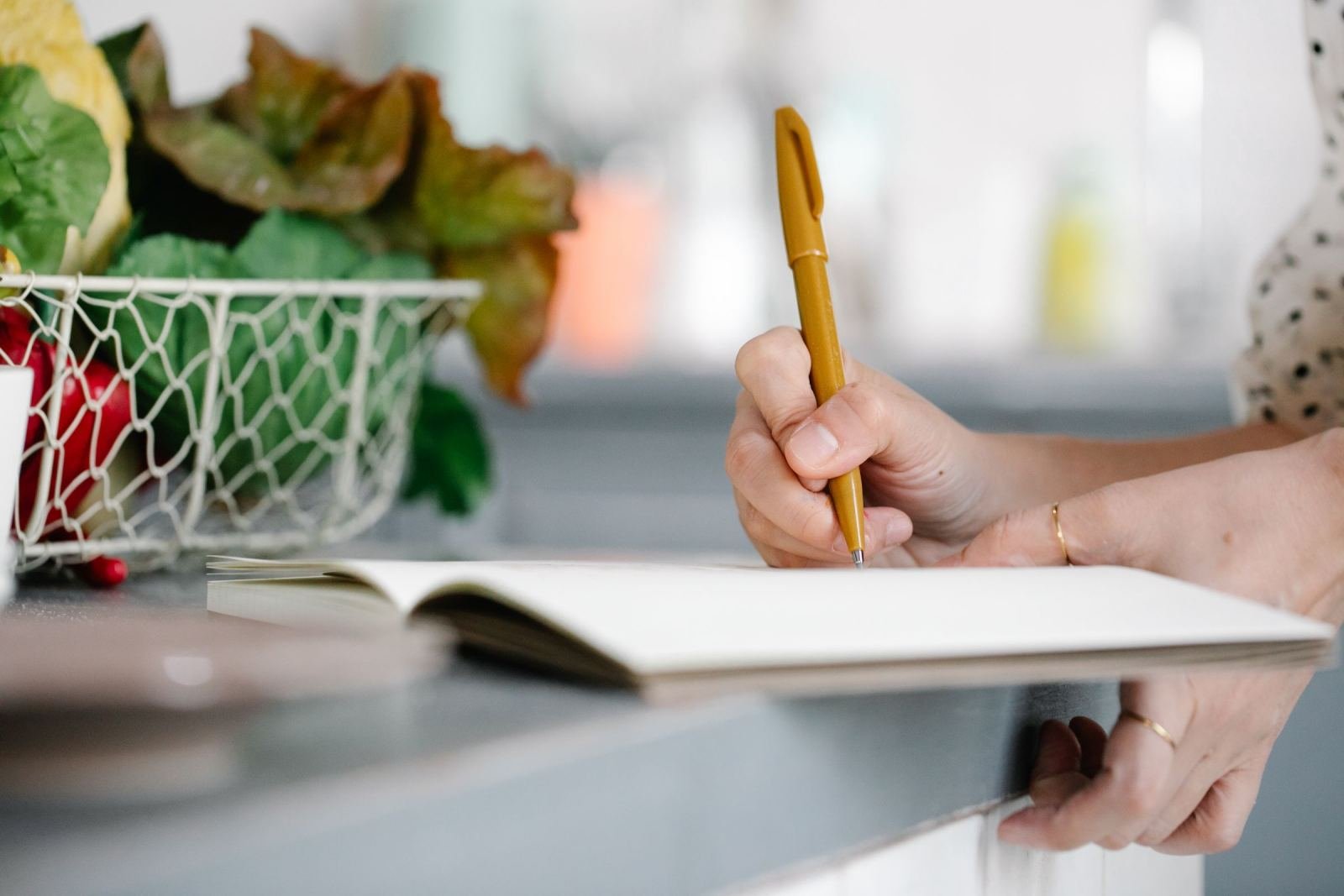 A person writes in a notebook with a yellow pen at a kitchen counter