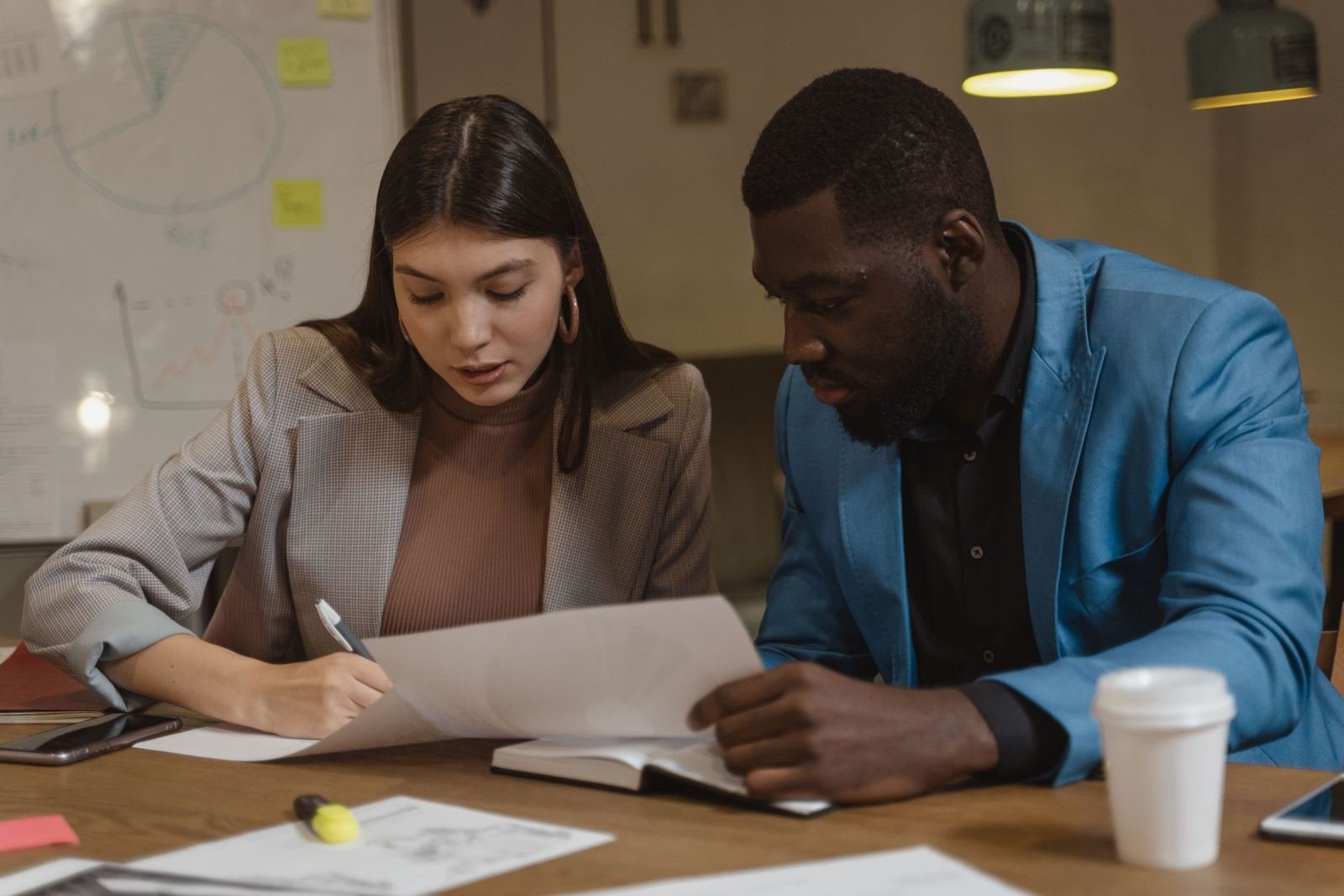 A woman and a man in professional attire review a document together at a desk