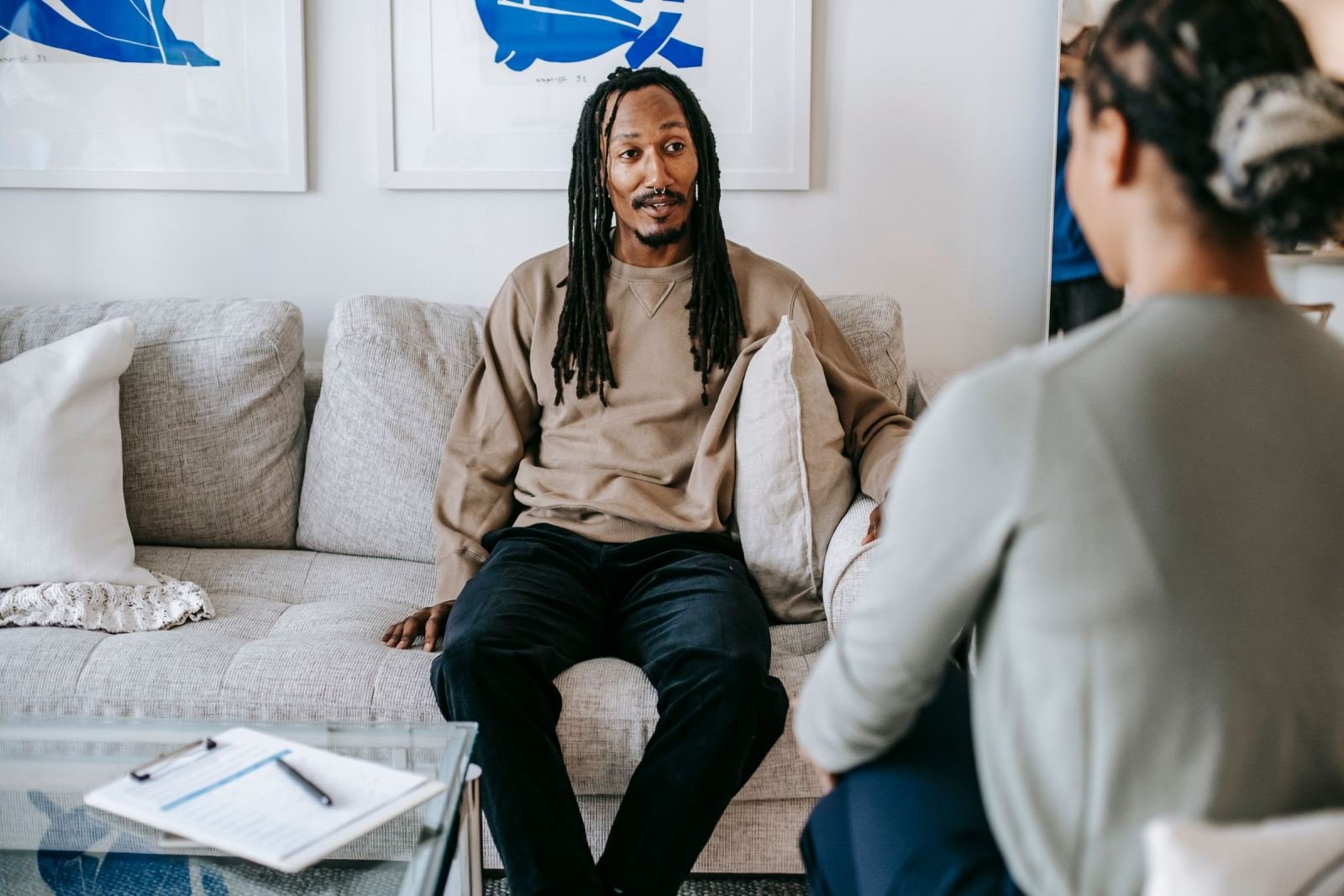 A man sits on a sofa and talks with a counselor in a bright office