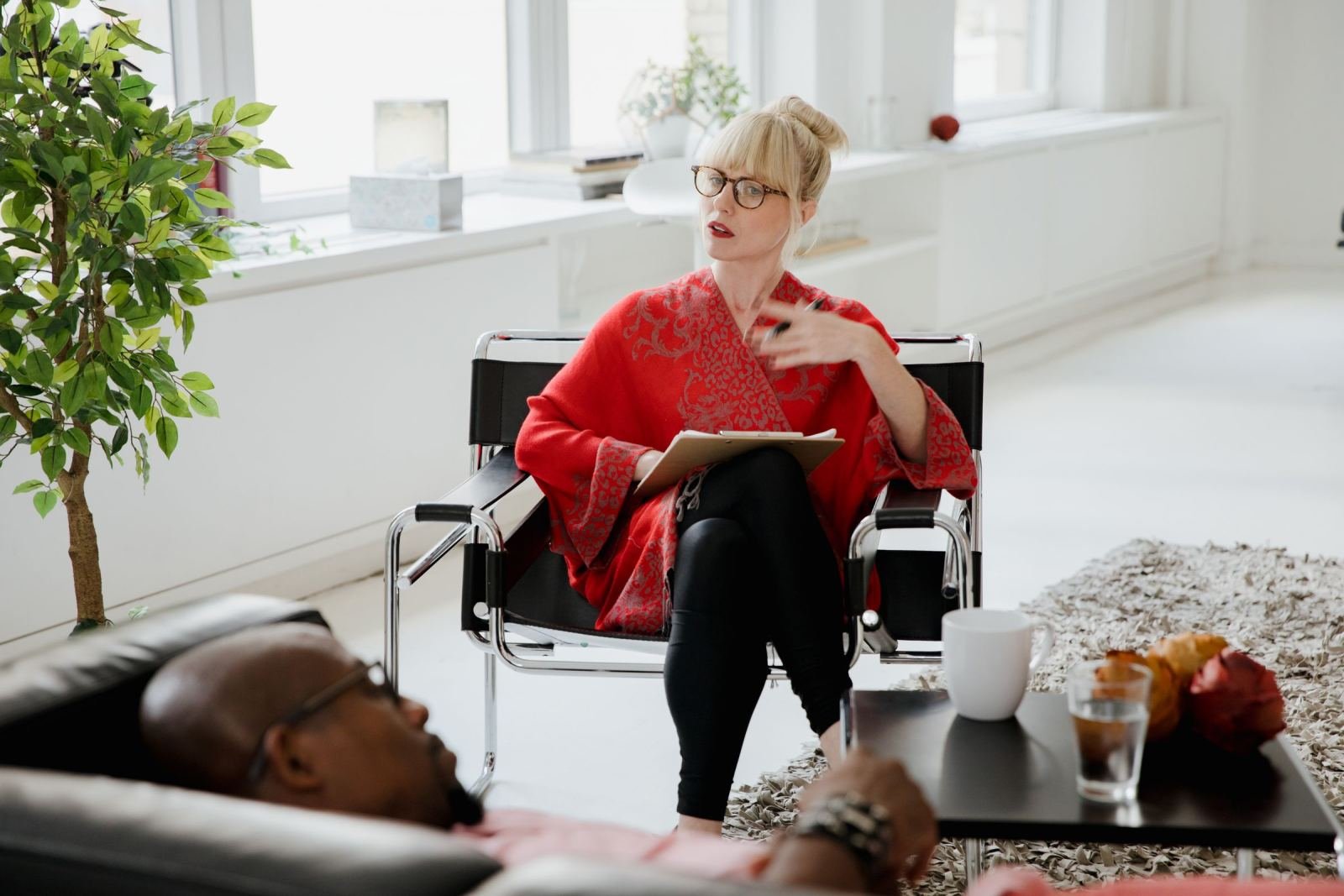 A woman with a clipboard speaks to a man reclining on a leather sofa