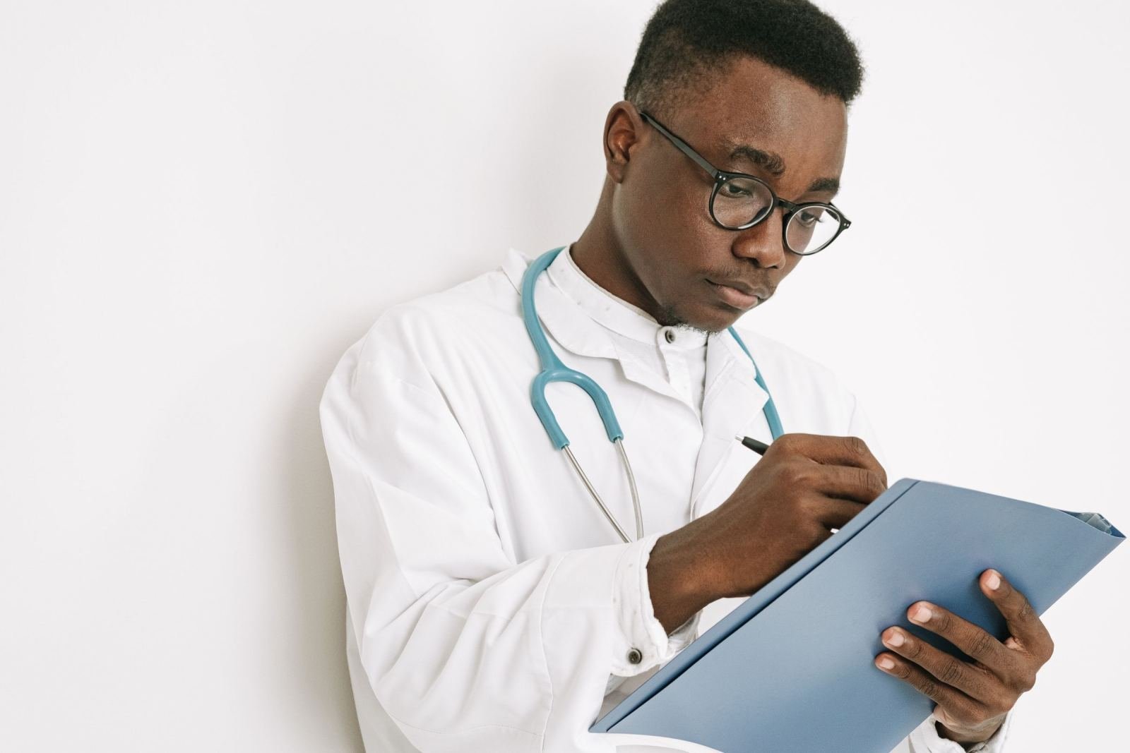 A doctor in a white coat and stethoscope writes on a blue clipboard
