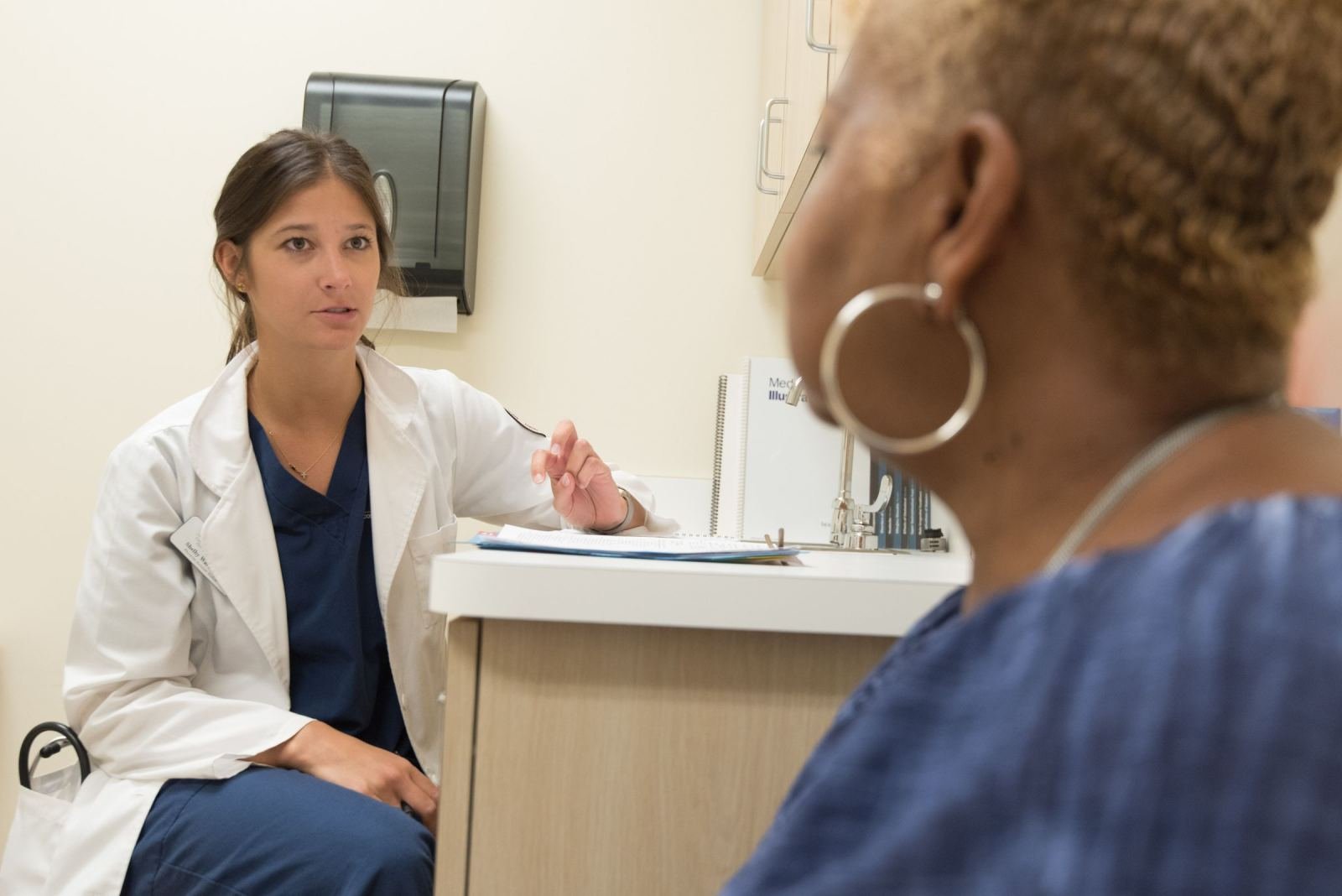 A healthcare provider in a white coat talks with a patient in a bright office