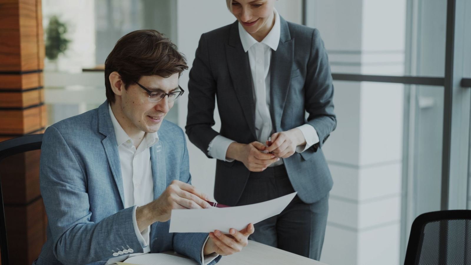 Two people in business clothes look over a paper in an office.