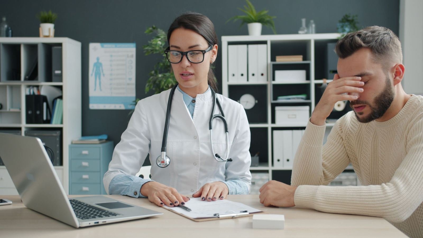 A clinician in a white coat reviews a care plan with a man at a desk
