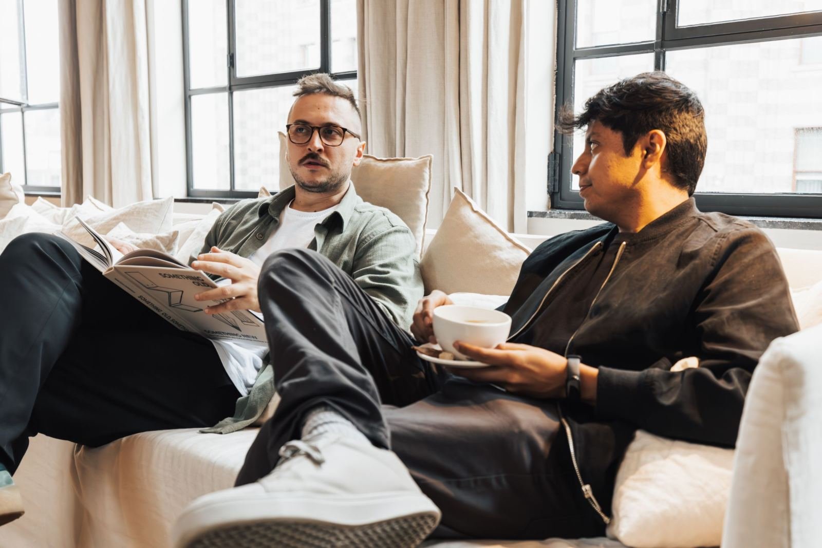 Two men sit on a white couch in a well-lit room