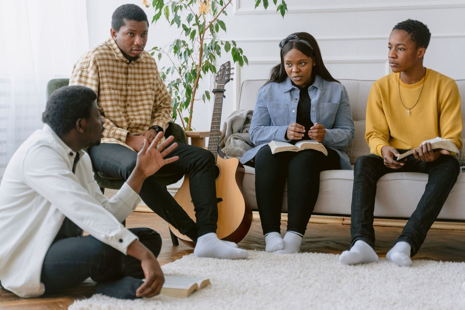 Four people sit in a circle in a living room, talking and holding books