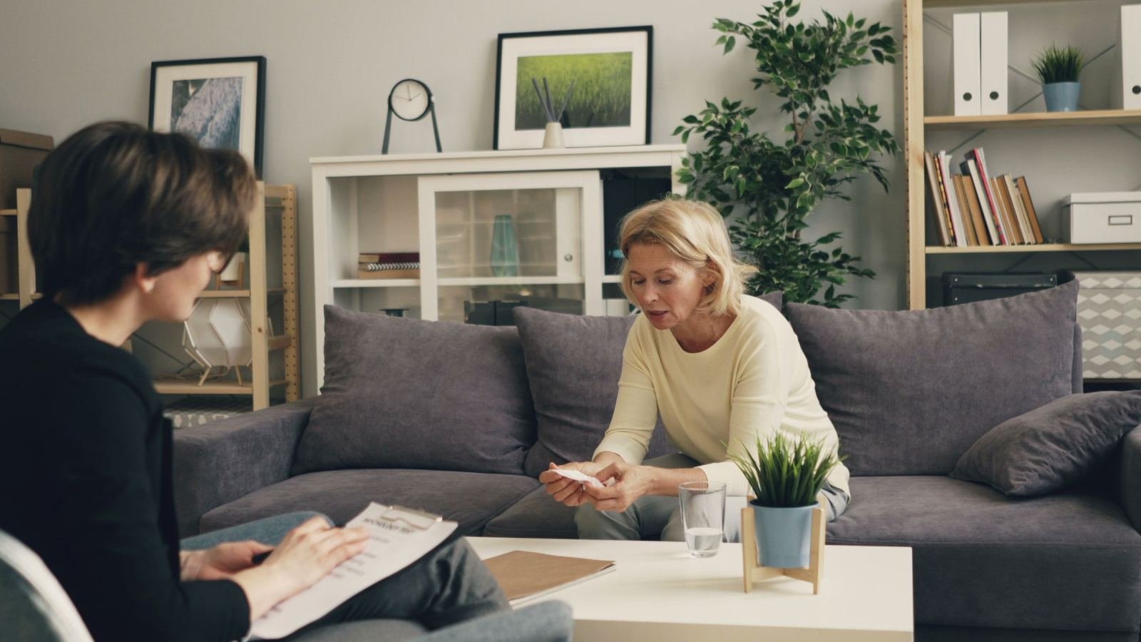 A woman on a sofa speaks with a professional holding a clipboard