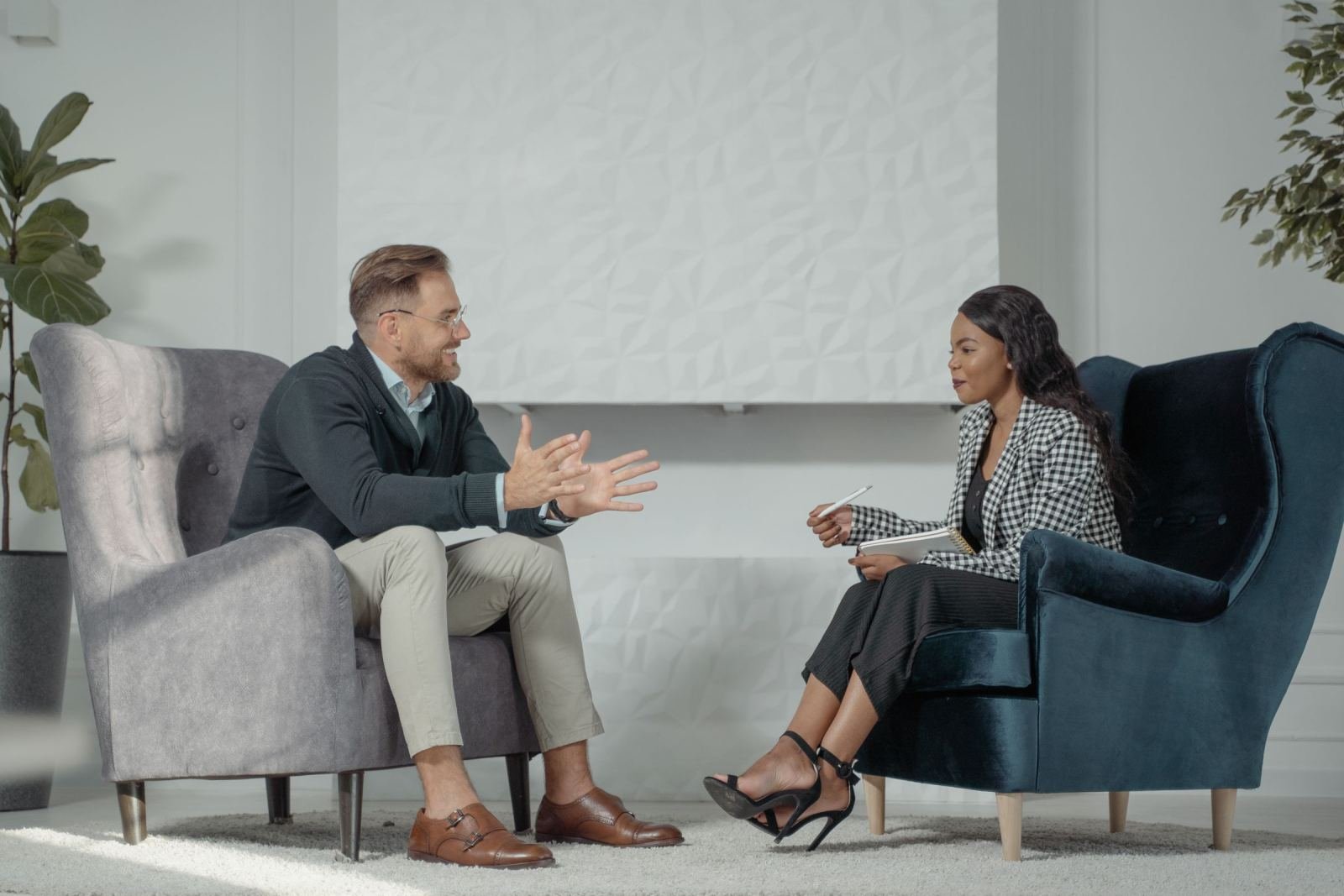 A man and a woman talk while sitting in armchairs in a bright office