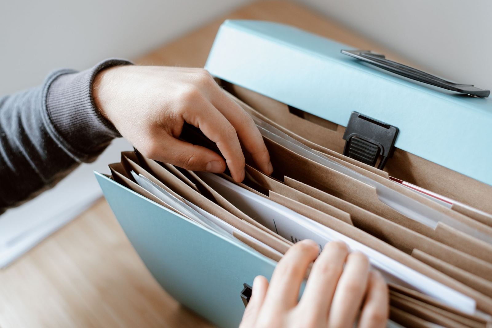 A person's hands sorting through brown folders in a light blue expanding file folder