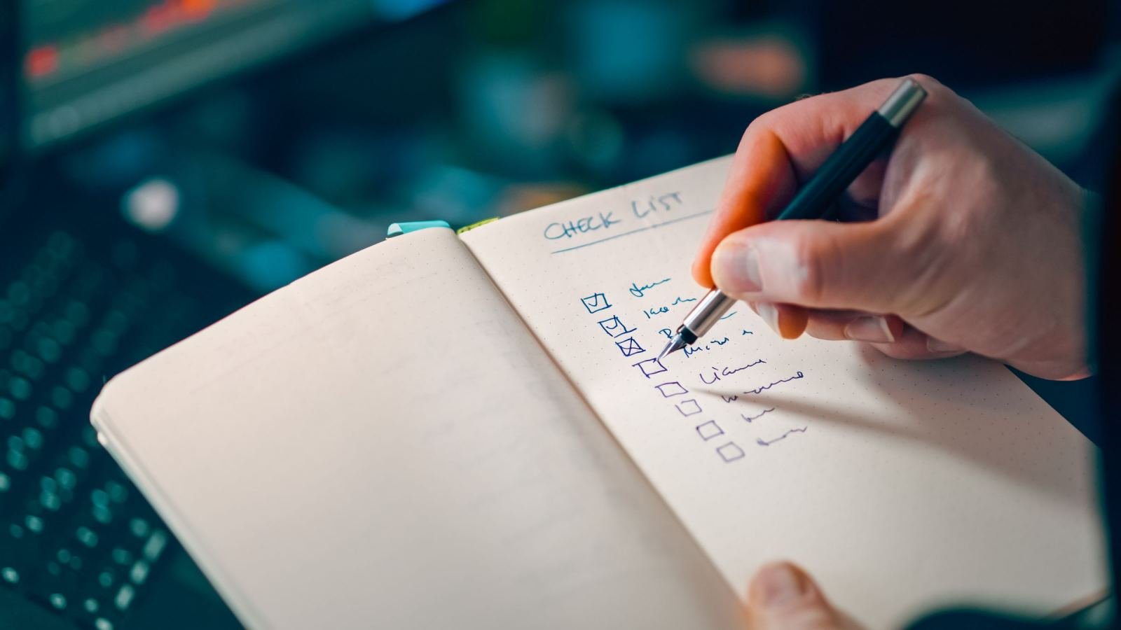 A hand marks items on a handwritten list in a notebook