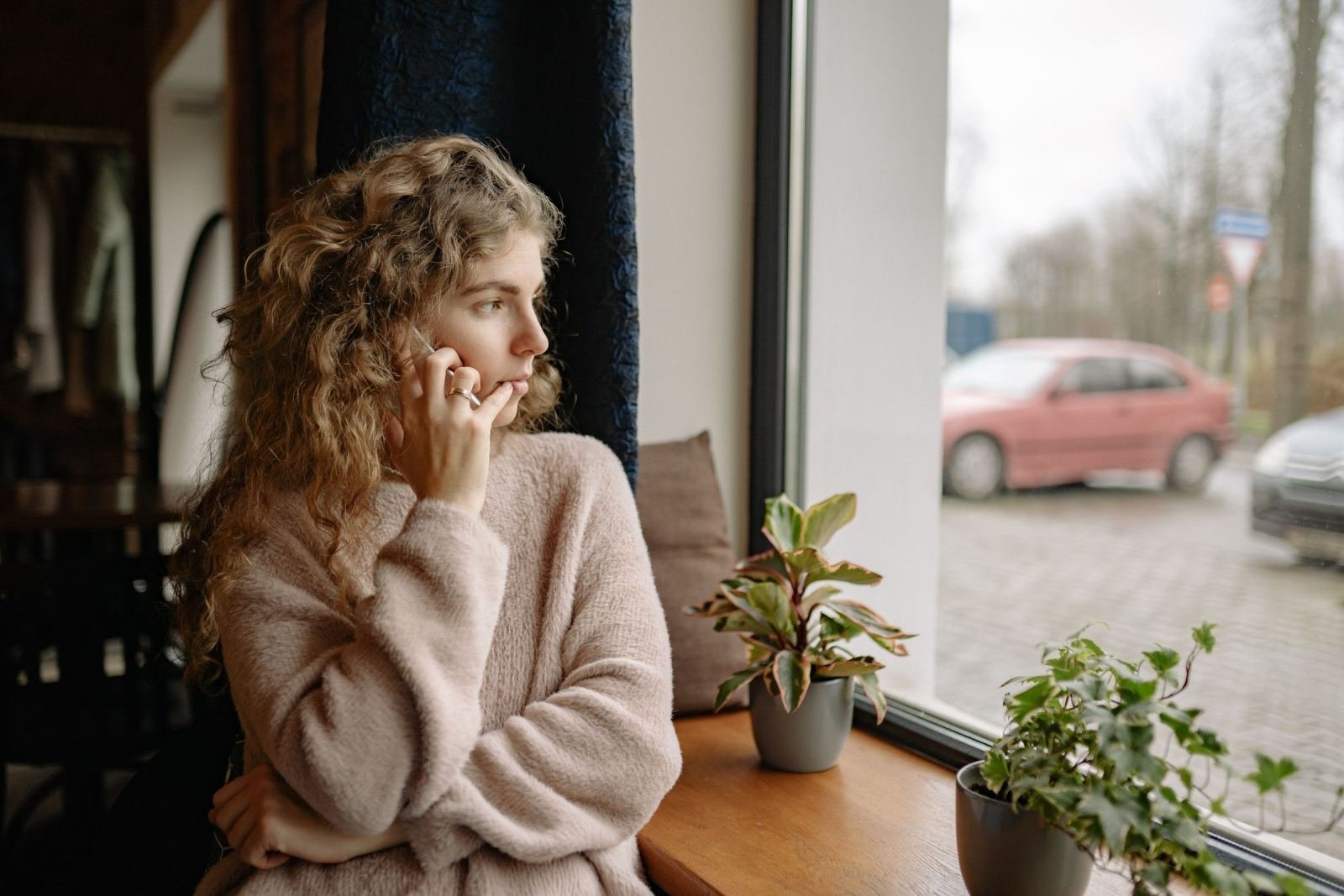A woman in a beige sweater makes a phone call while looking out a window