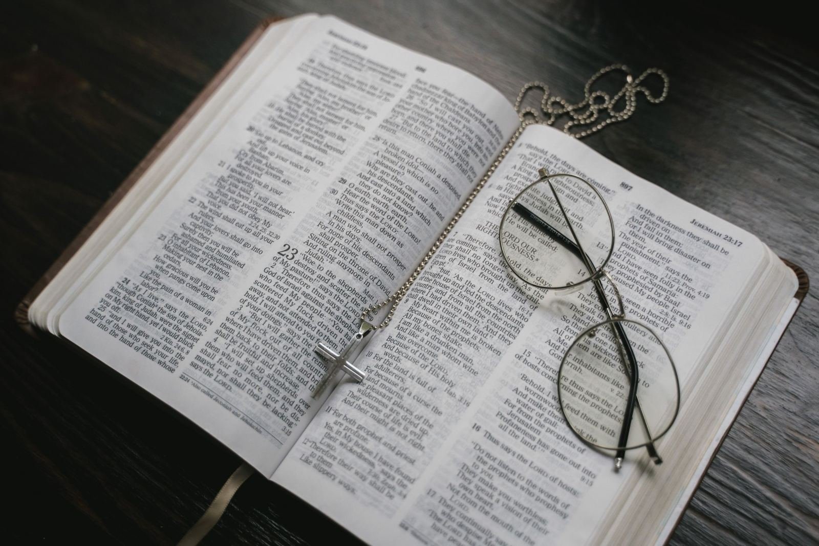 An open book with eyeglasses and a beaded necklace resting on the pages