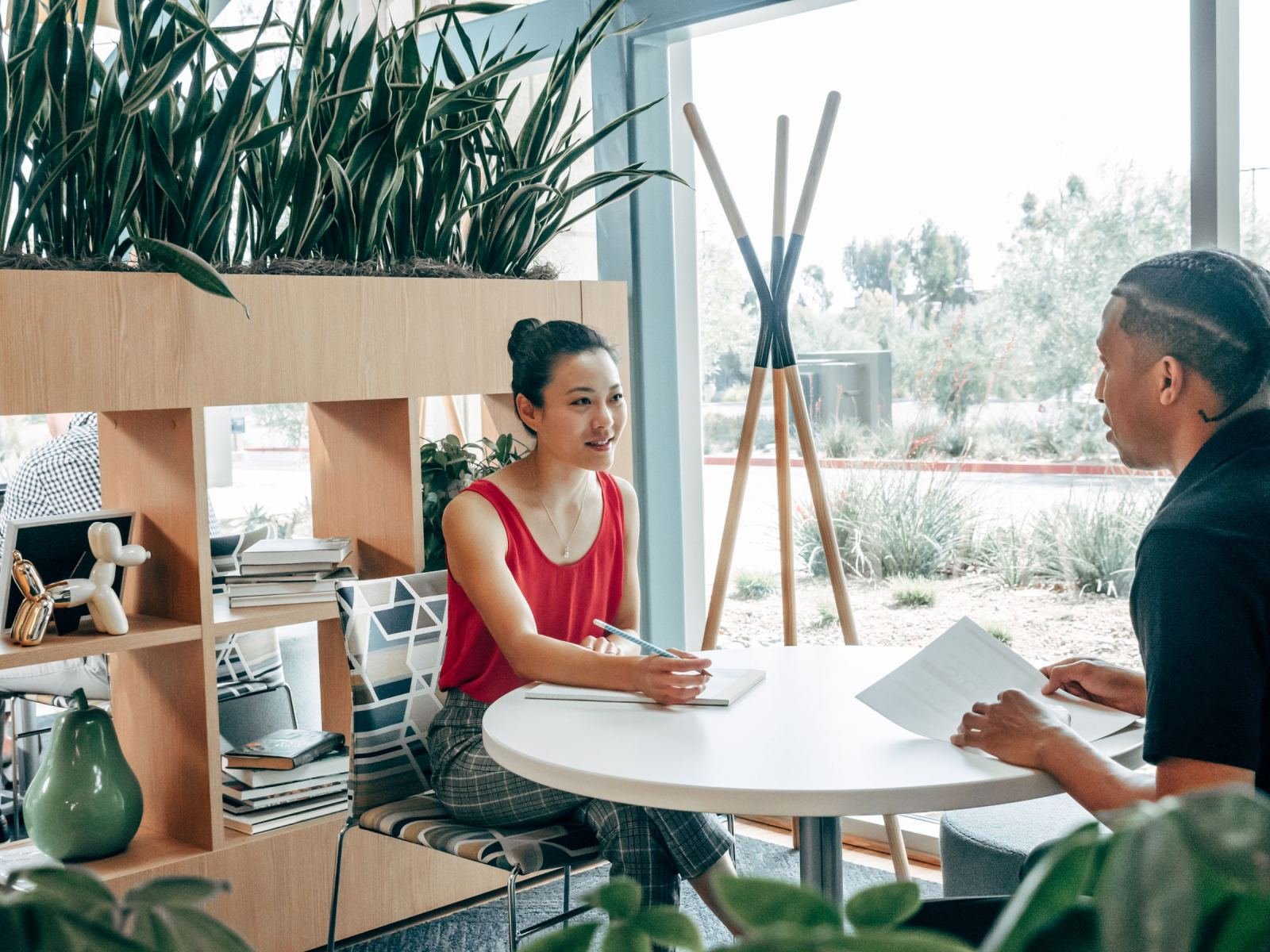 A woman and a man sit at a round table in a bright office discussing a document