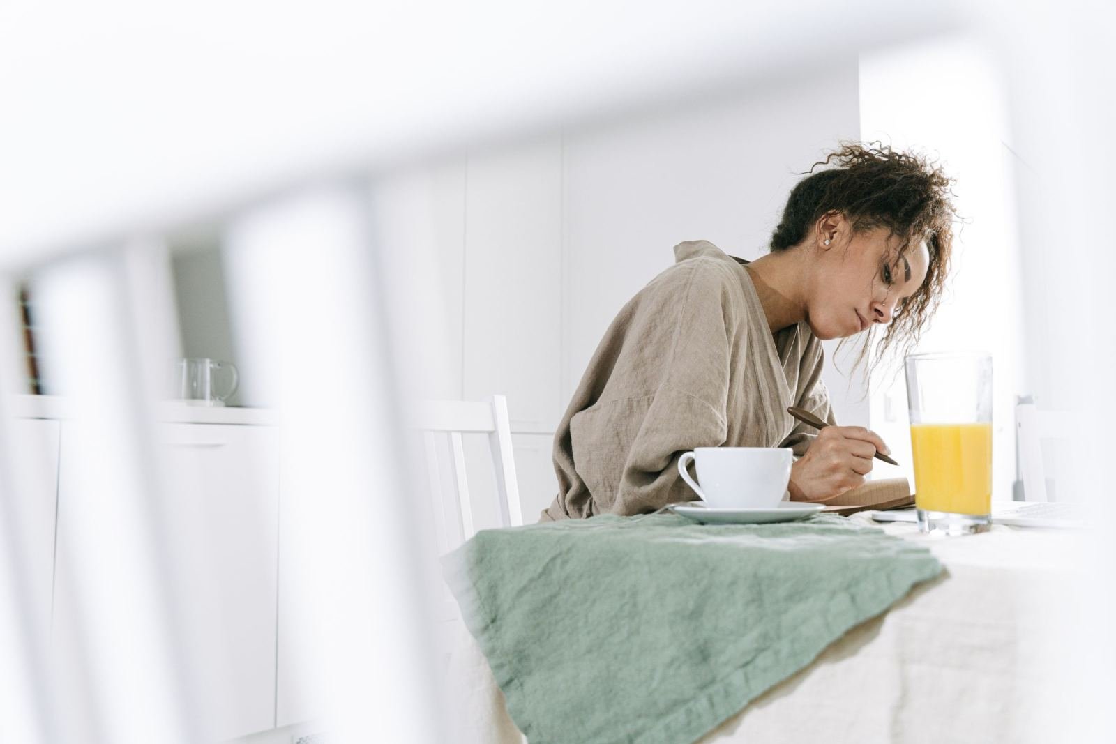 A woman writes in a notebook at a table with a cup of coffee and orange juice