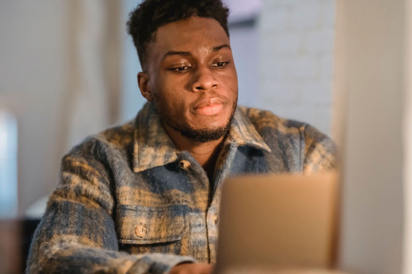 A man in a plaid shirt looks at a laptop screen