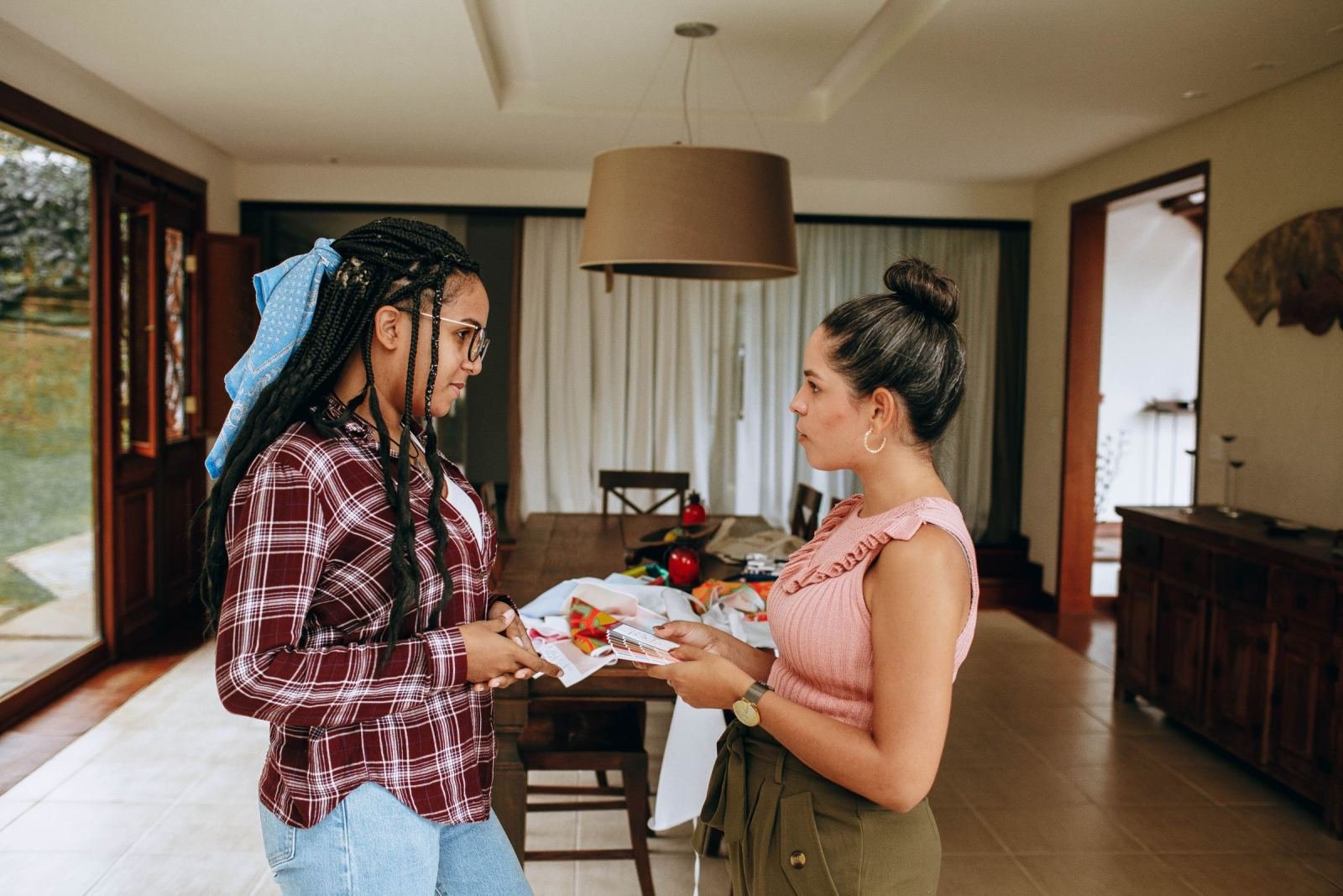 Two women talk in a dining room while one holds a stack of folded clothes