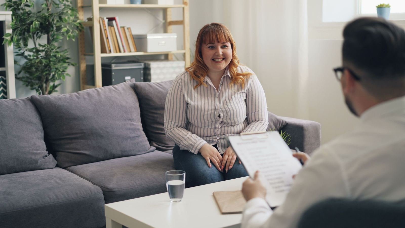 A professional with a clipboard talks to a smiling woman in an office.