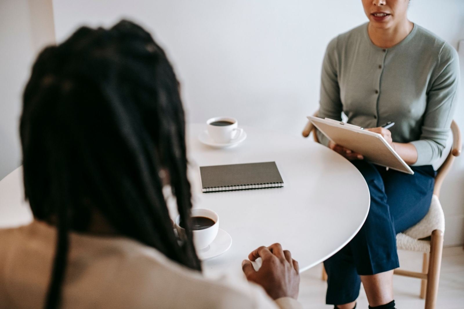 A counselor with a clipboard talks to a client across a white table