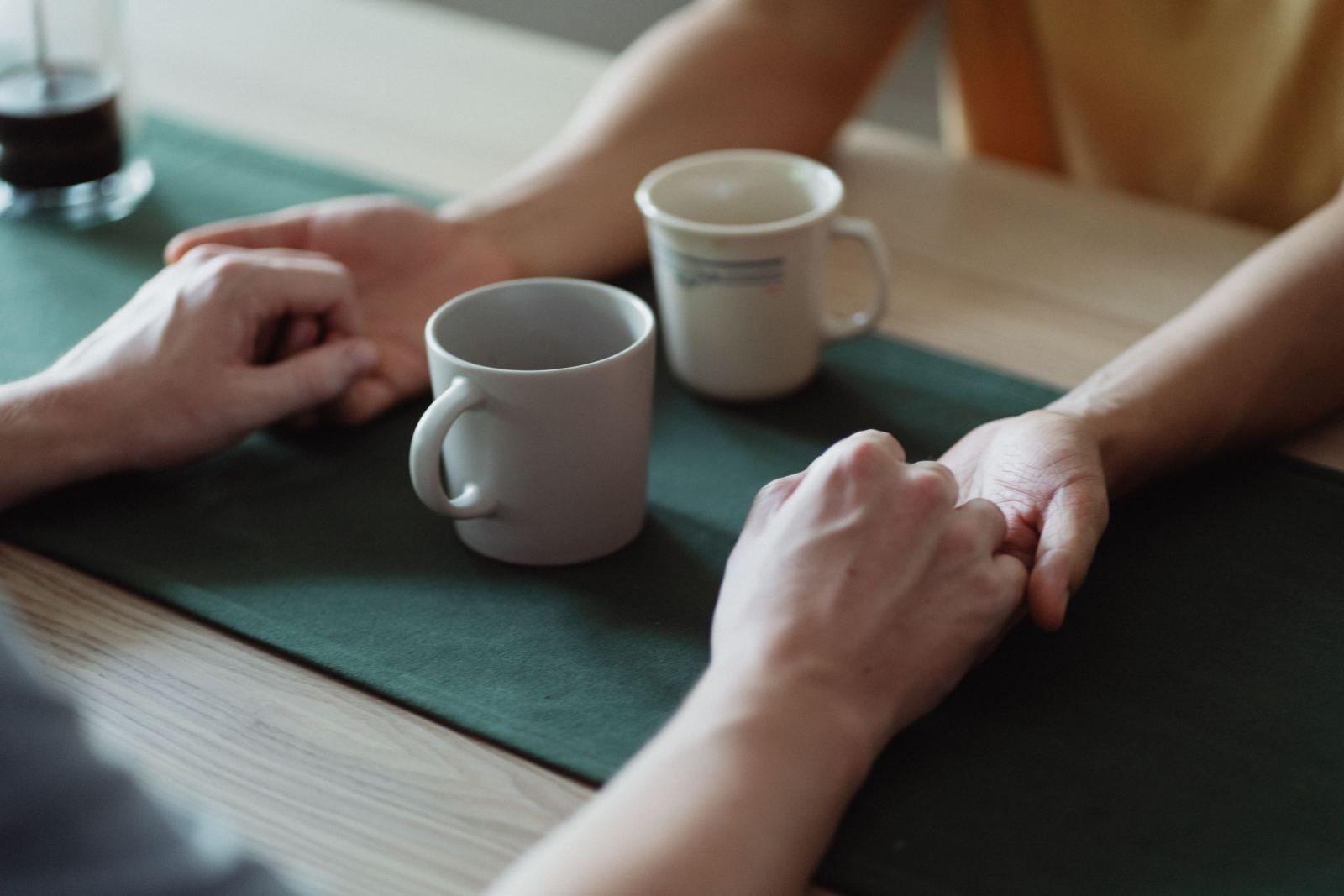 Image of two people holding hands over a table with coffee cups