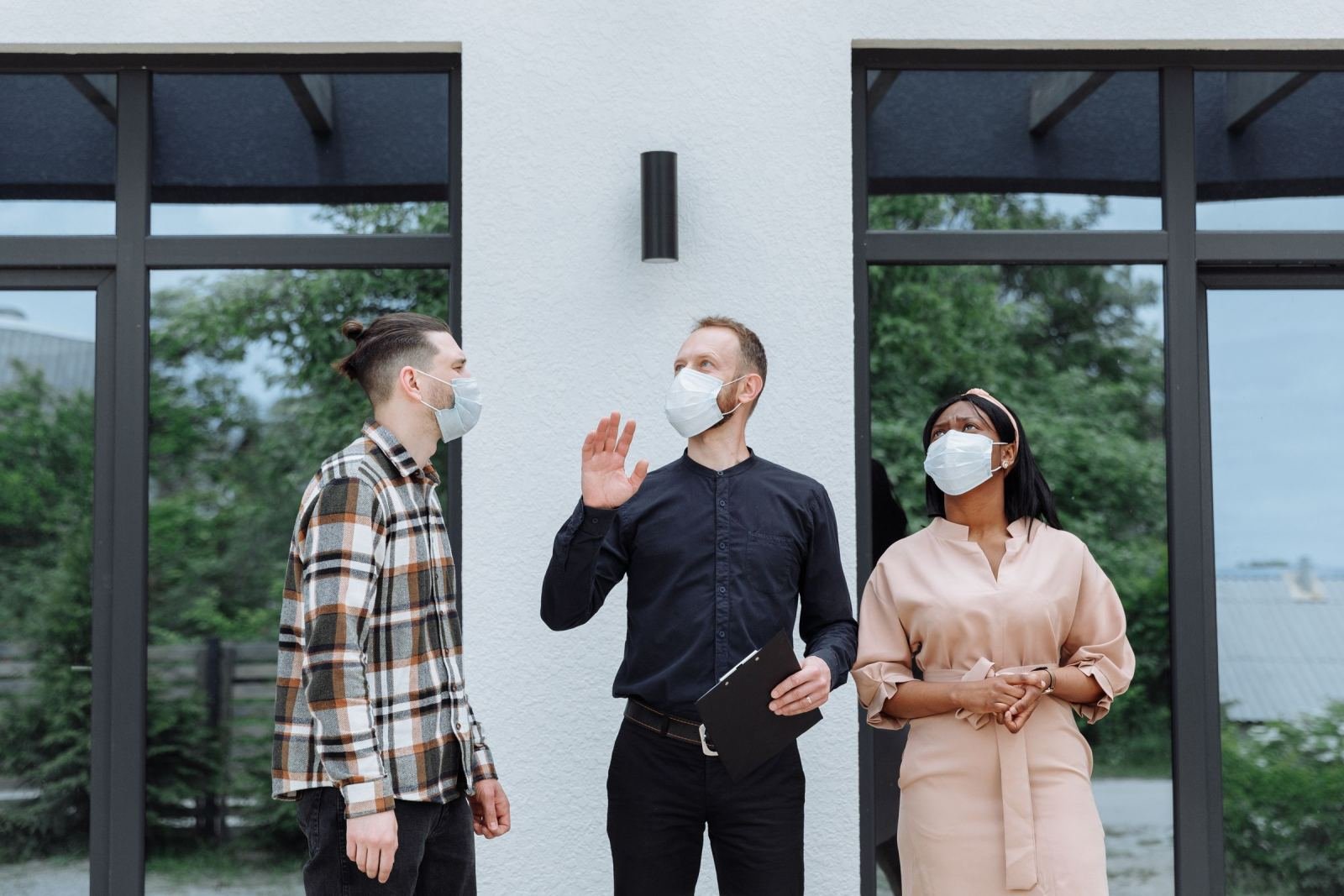 Three people wearing face masks stand outside a building with large windows