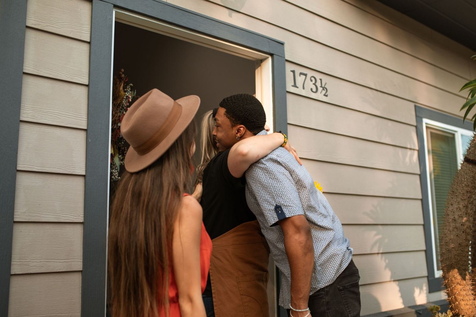 A man and woman hug in the doorway of a house while another woman looks on